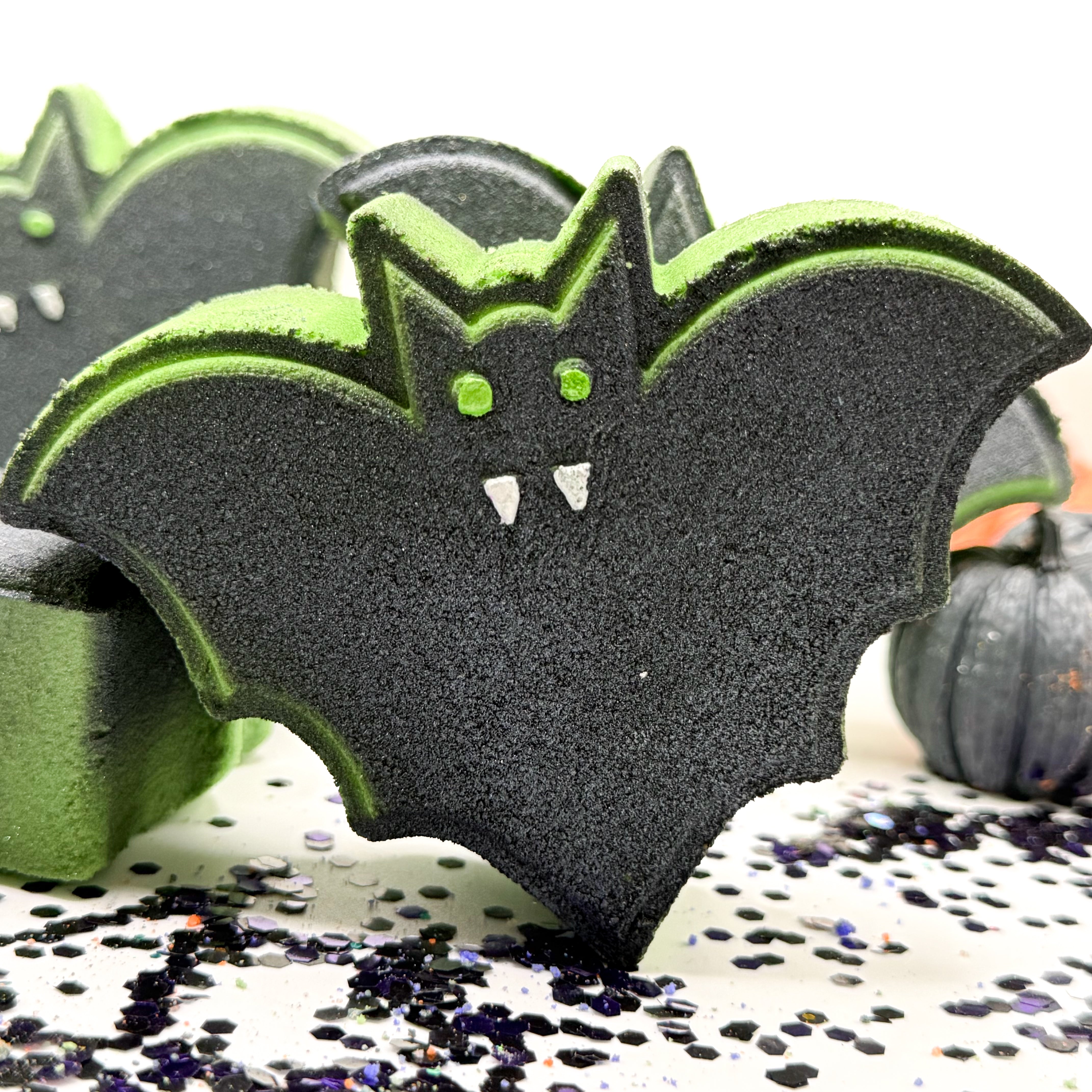 A green bat shaped bath bomb airbrushed black. Hand-painted green eye and white fangs by Rusted Acre Soap Co.