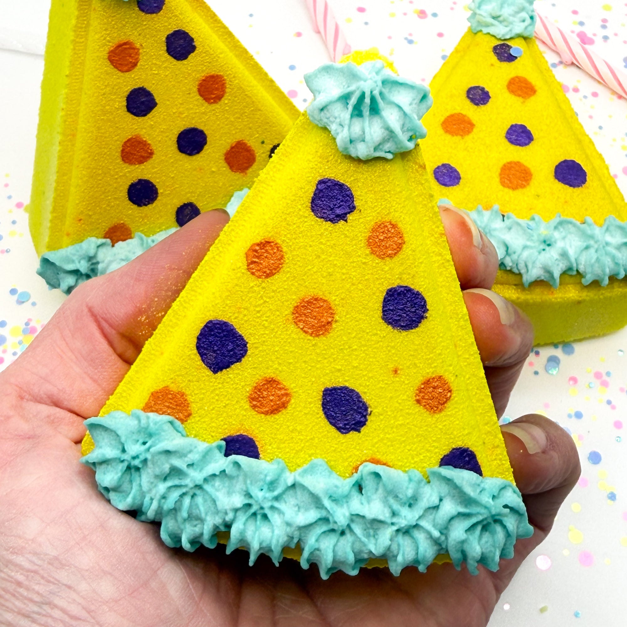 One yellow birthday hat shaped bath bombs with hand painted polka dots held in an hand.