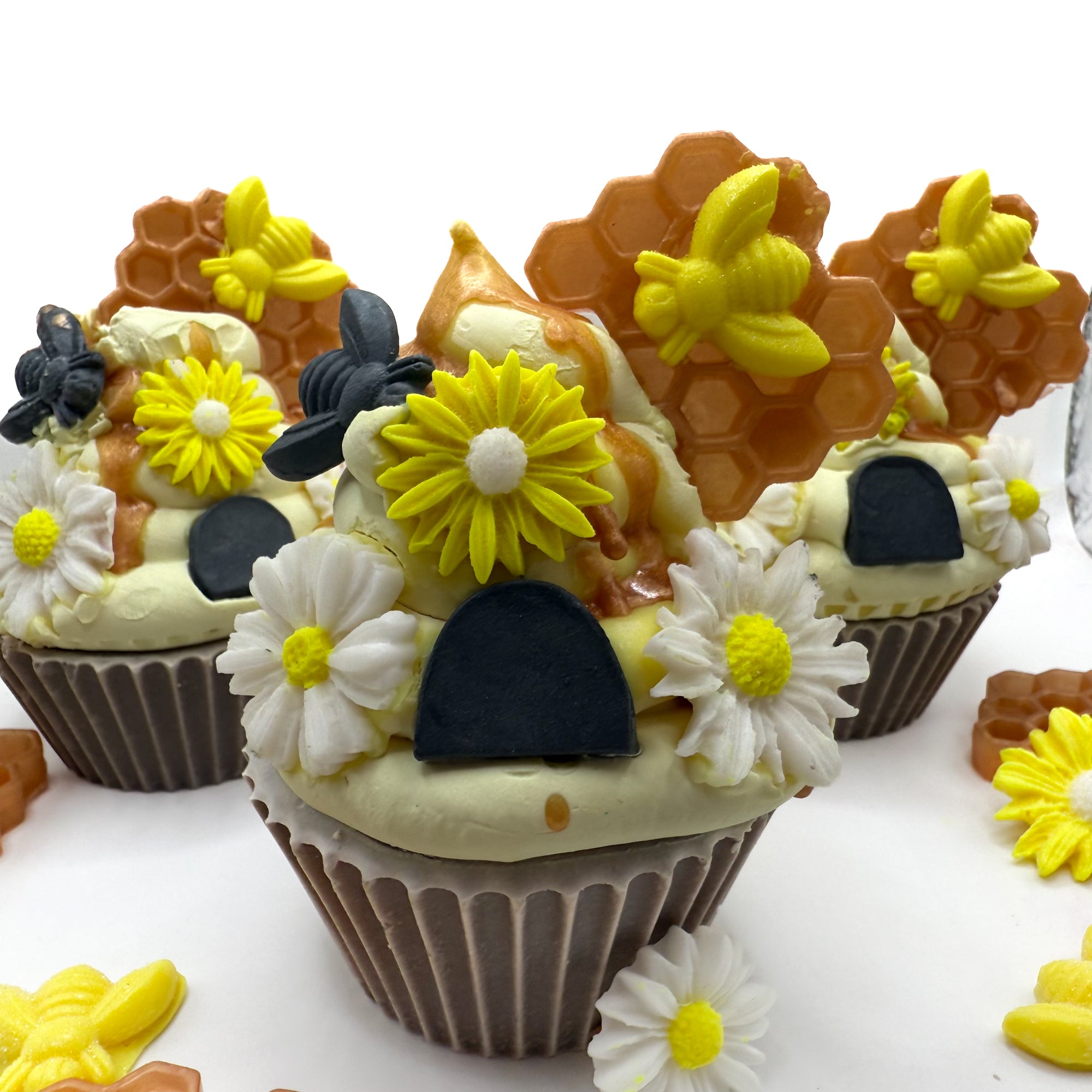 Beehive cupcake soaps with hand-piped frosting and soap embellishments including honeycomb, bees, and daisies, scented with Wildflower & Honey.