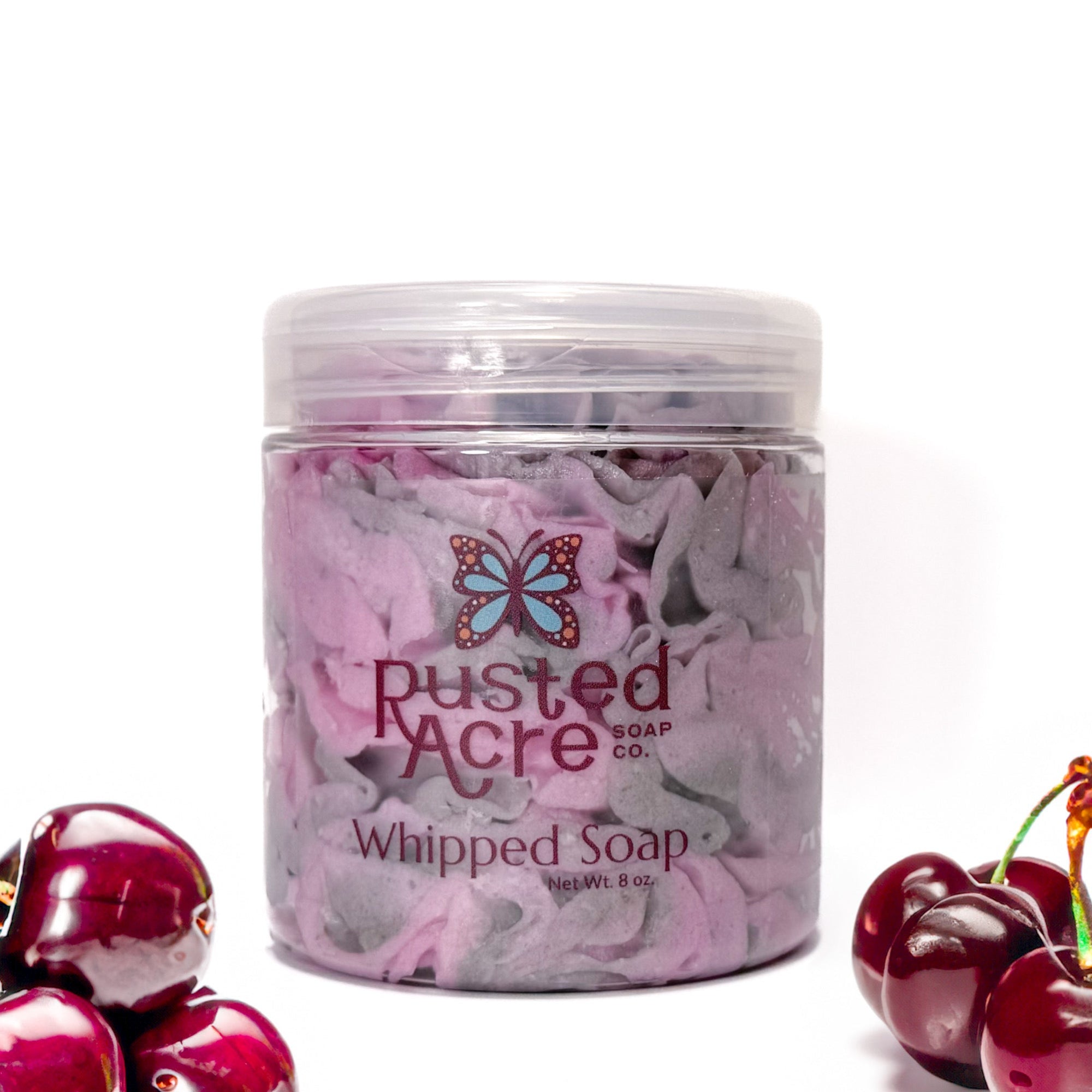 Jar of Rusted Acre Soap Company's vegan black cherry whipped soap. Pink and Gray soap in a reusable plastic jar in a lifestyle setting.
