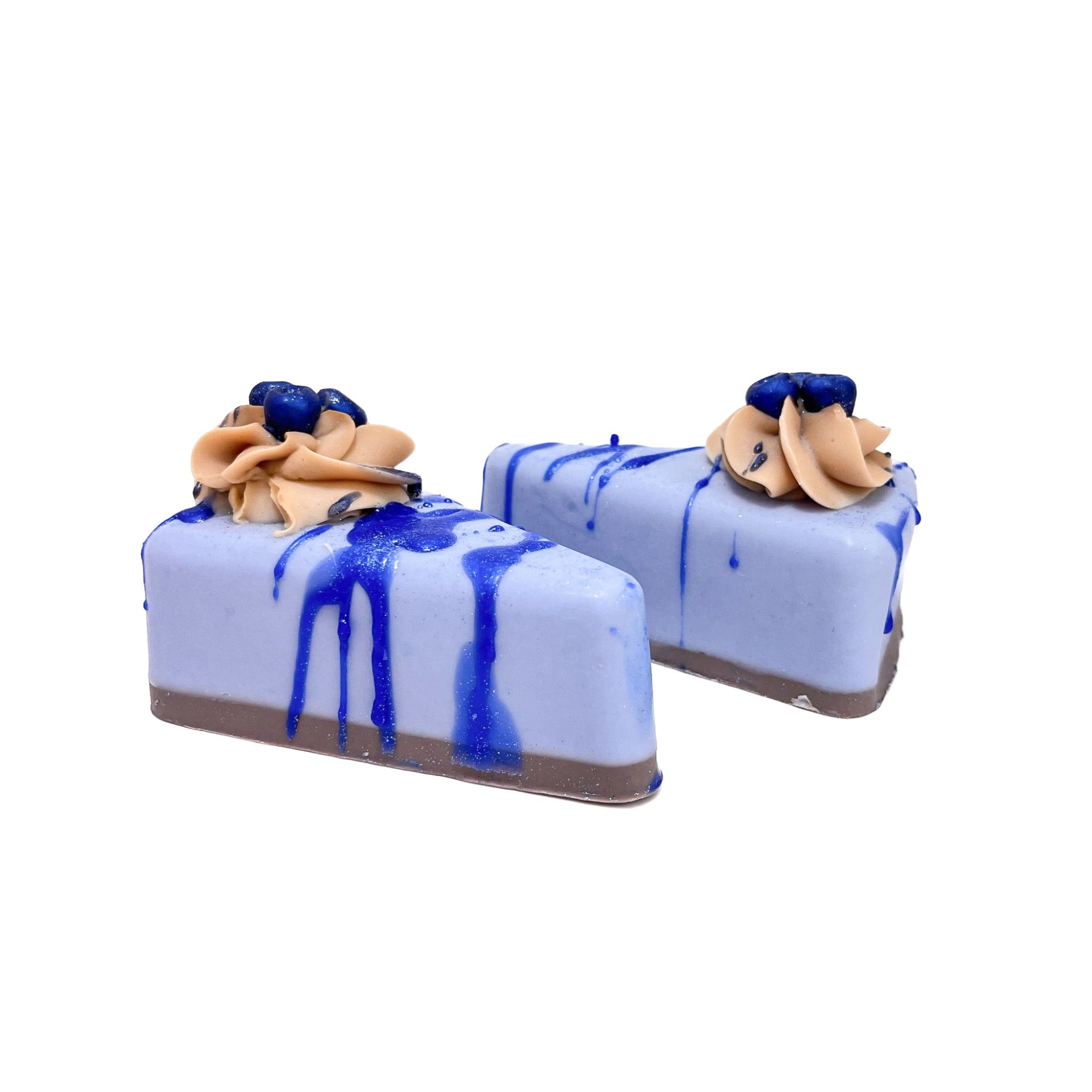 Two slices of light blue pie shaped soap. Topped with a puff of cream colored cold process soap and blueberry soaps.