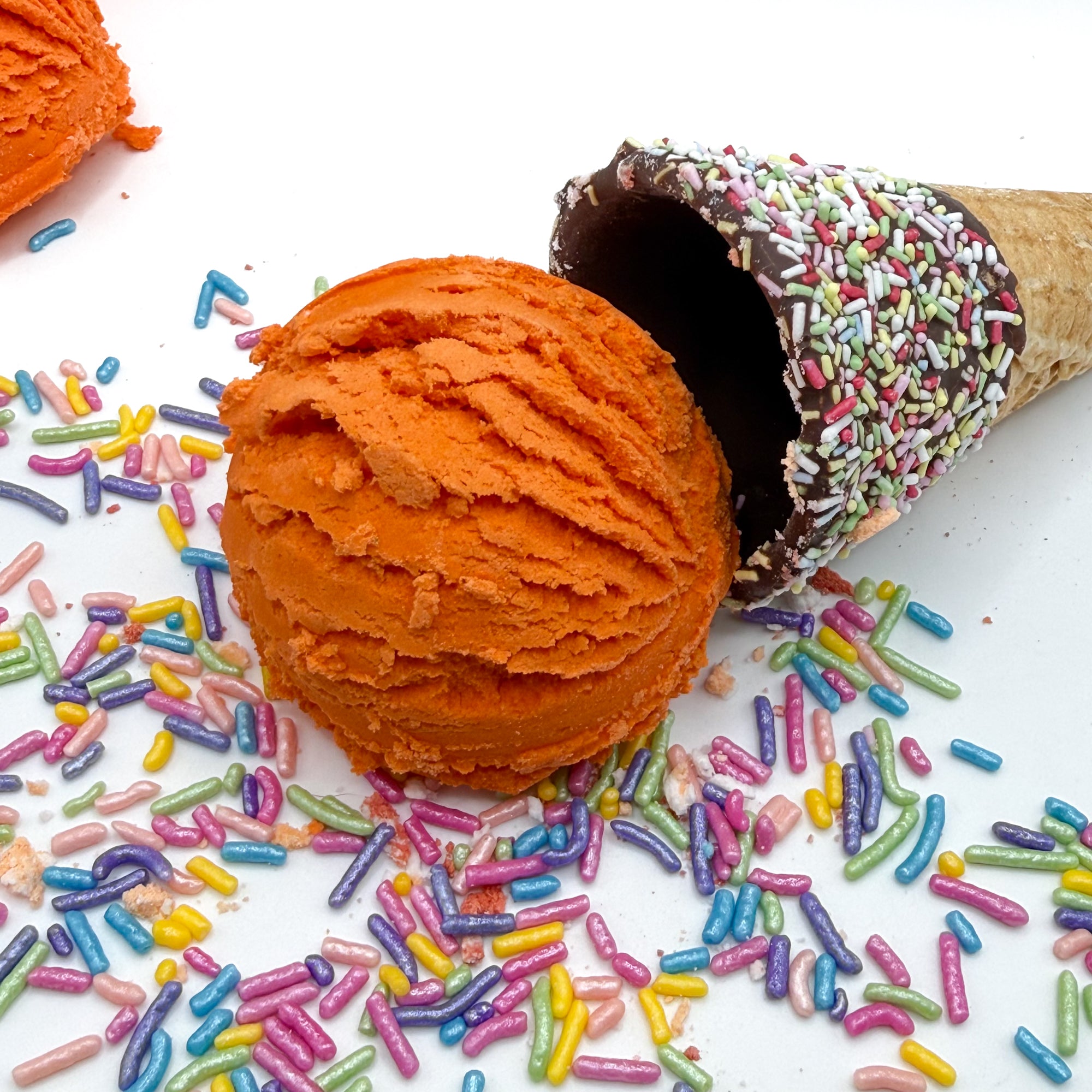 One orange pumpkin spice scented bubble bath scoop handmade by Rusted Acre Soap Co. Scoop looks like an ice cream scoop. White background with sprinkles and ice cream cone prop on a white background.