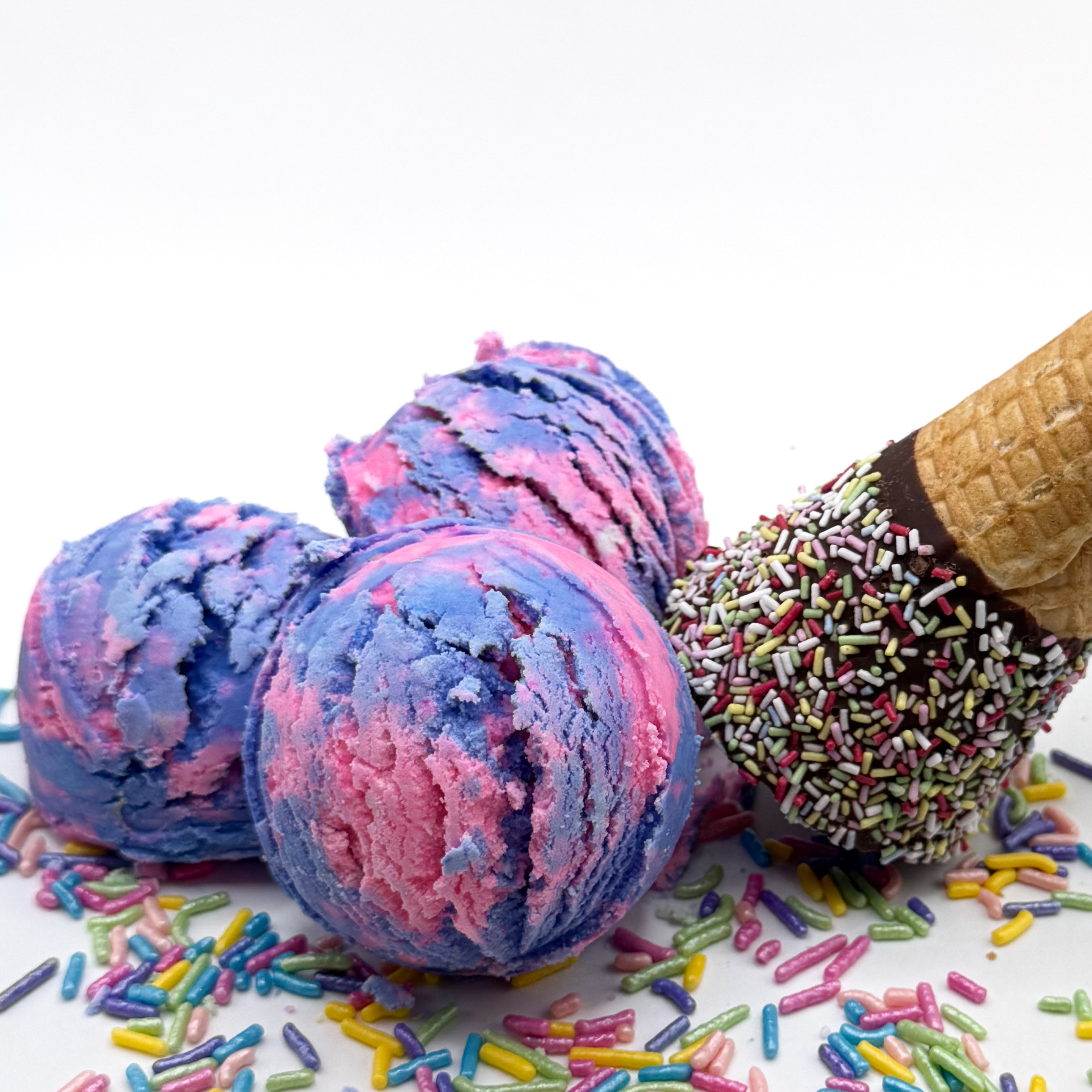 Three pink and purple raspberry vanilla scented bubble bath scoops that look like scoops of ice cream on a white background with sprinkles and an ice cream cone