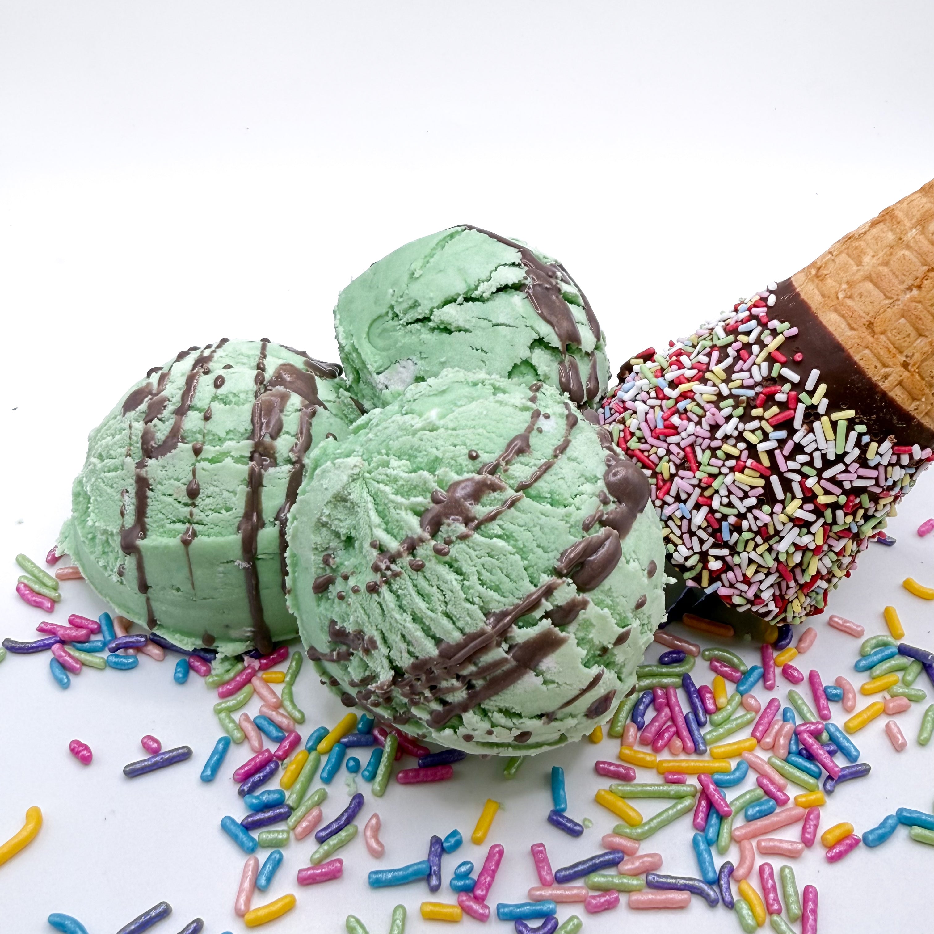 Three mint green with brown drizzle bubble bath scoops scented with mint chocolate chip Bubble scoops are hand made by Rusted Acre Soap Co and look like scoops of ice cream on a white background with sprinkles and an ice cream cone