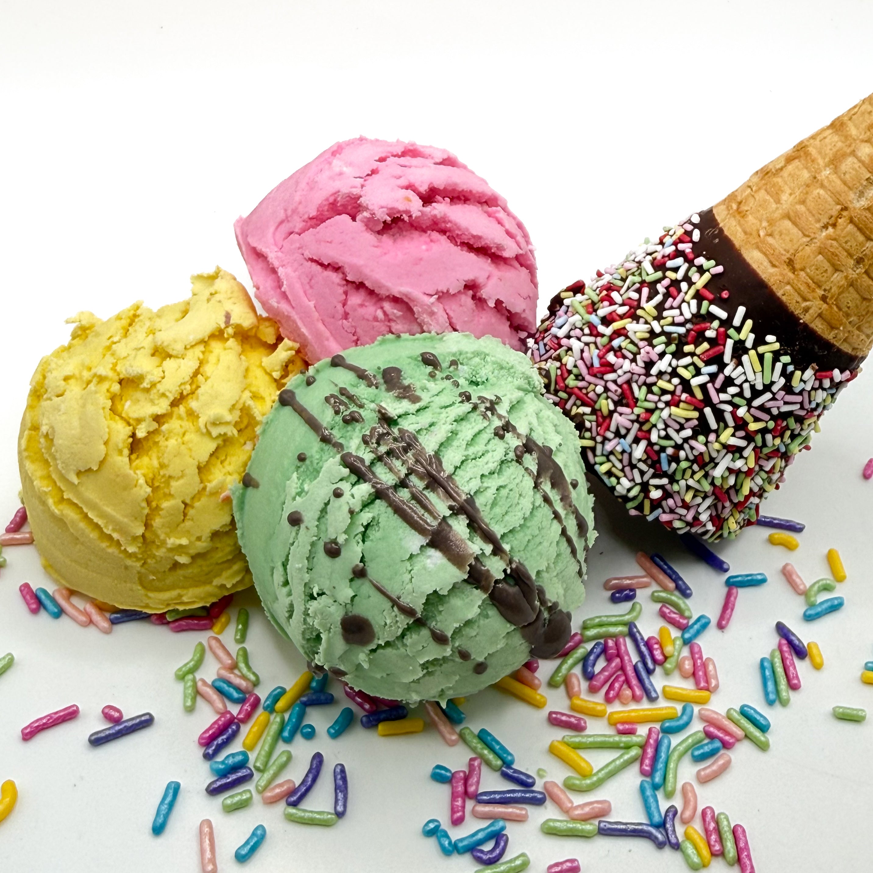 Three mixed colored and scented bubble bath scoops for a surprise scoop option. The hand made bubble bath scoops that look like scoops of ice cream on a white background with sprinkles and an ice cream cone