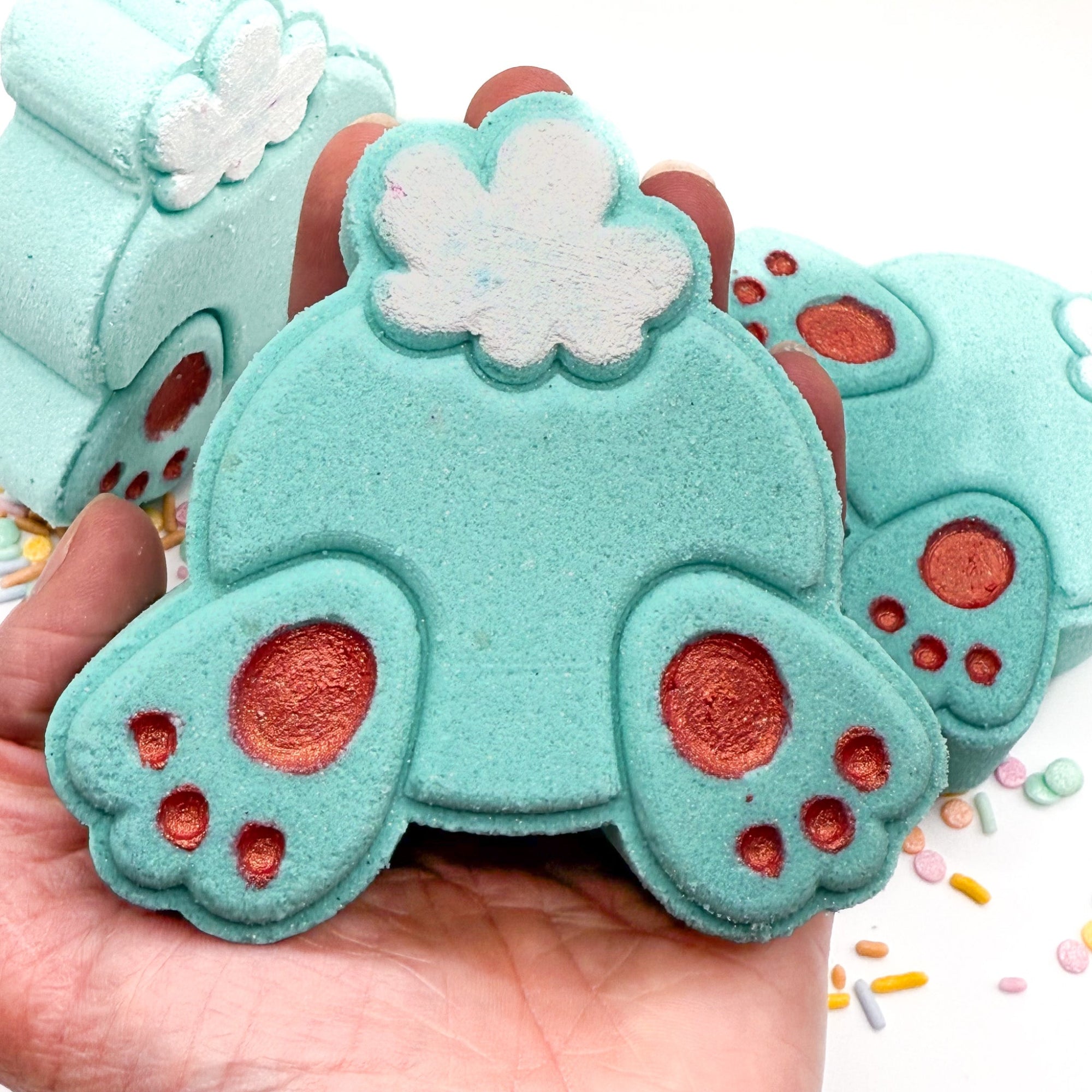 Teal bunny but bath bomb made by rusted acre soap company, front view in hand.