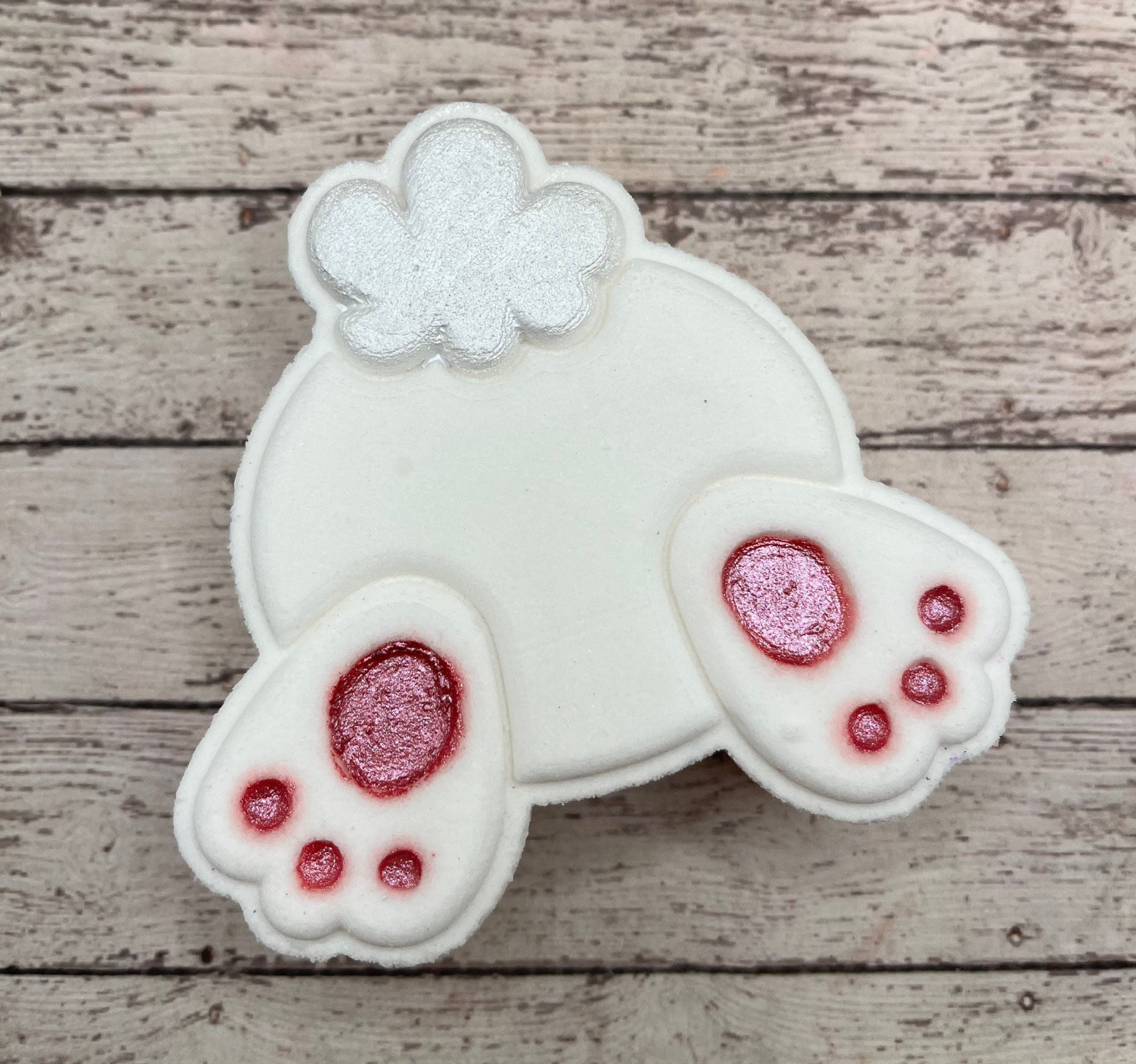 One white bunny butt shaped bath bomb from Rusted Acre Soap Co. The pads of the feet are hand-painted pink and the tail is shimmery..