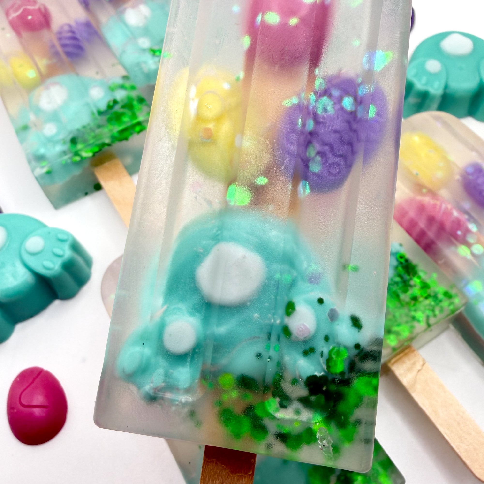 Up close view of a Easter popsicle shaped soap bar with a teal bunny butt and egg soaps embedded inside on a white background. Handmade by Rusted Acre Soap Co.