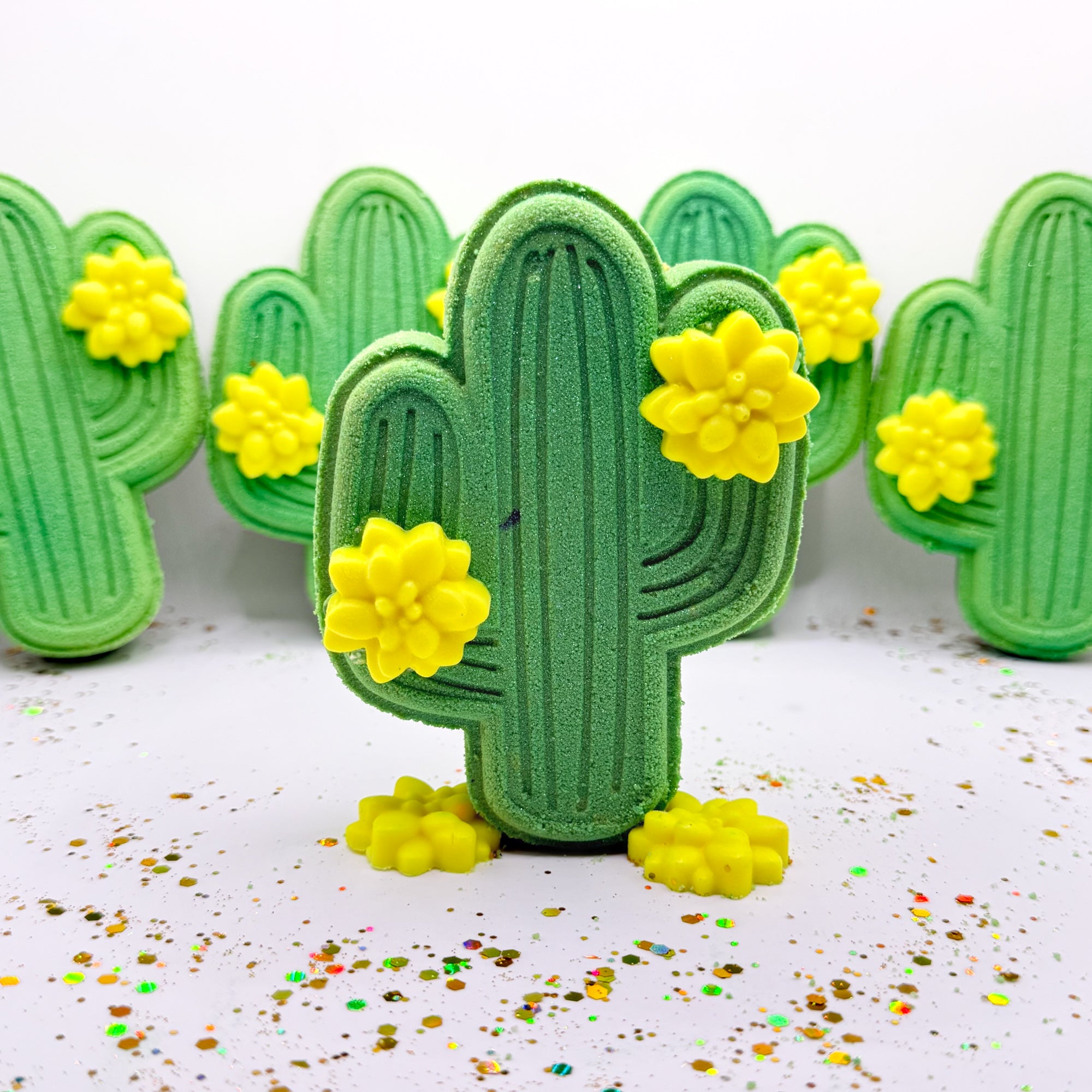 Multiple green cactus shaped bath bombs. Each adorned with two
light yellow cactus flower mini soap.