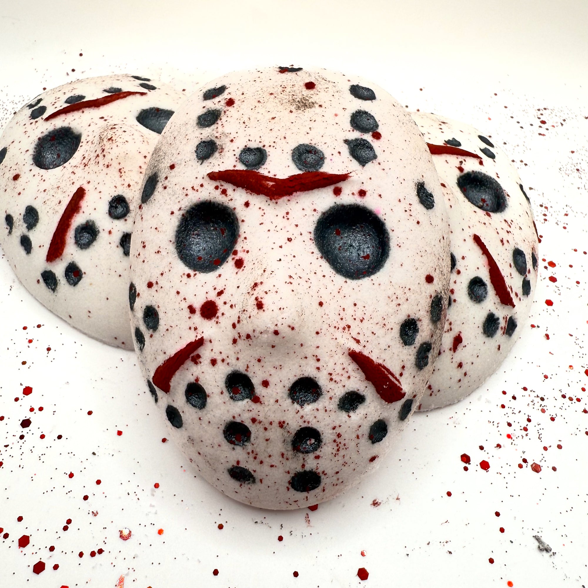 Group of Camp Slasher hockey mask bath bombs stacked together showing full mask details, blood splatter, and hand-painted black dot accents.