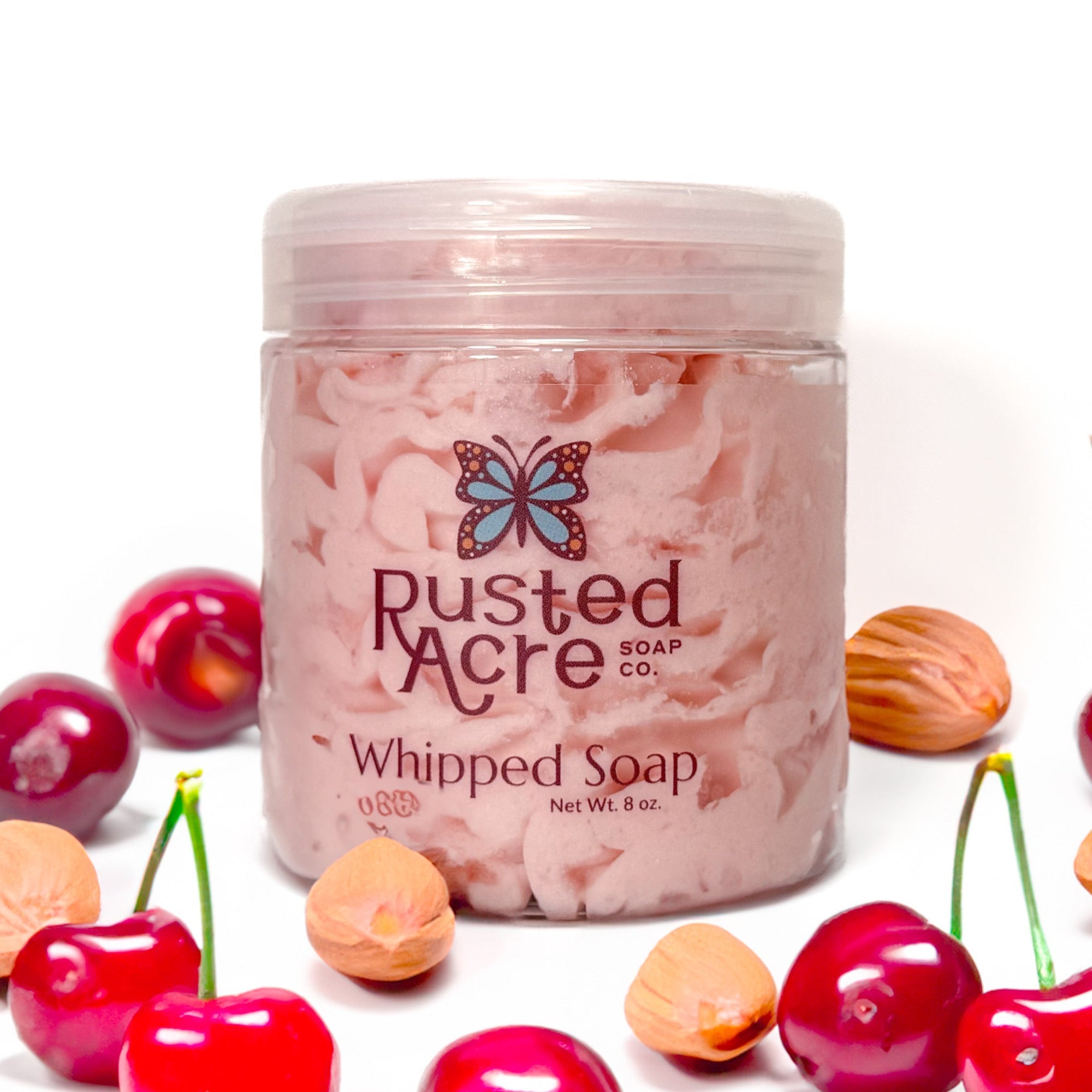 Jar of Rusted Acre Soap Company's vegan cherry almond whipped soap. Pink soap in a reusable plastic jar in a lifestyle setting.