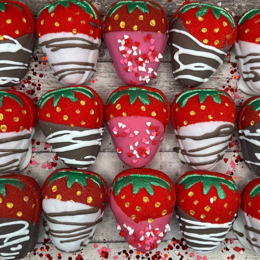 Decorative strawberry bath bombs with chocolate drizzle on a wooden surface.