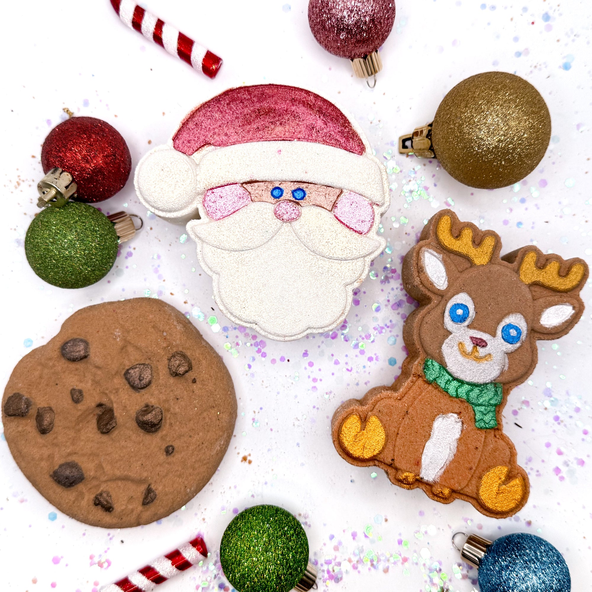 Christmas themed handmade premium bath bomb including a Santa Claus, reindeer, and chocolate chip cookie, surrounded by festive ornaments on a white background.