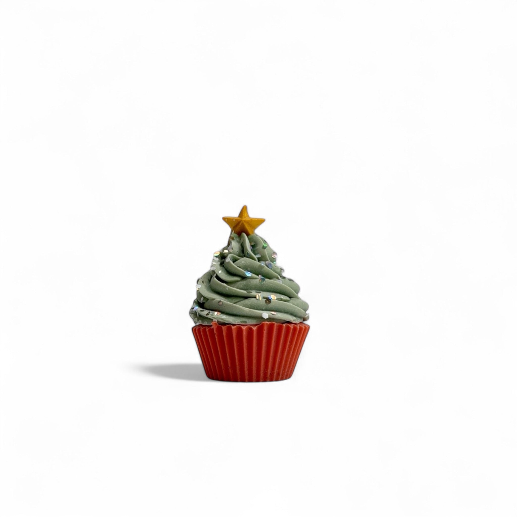 A Christmas tree themed cupcake soap with white sprinkles handmade by Rusted Acre Soap Co. Red cake topped with green frosting.