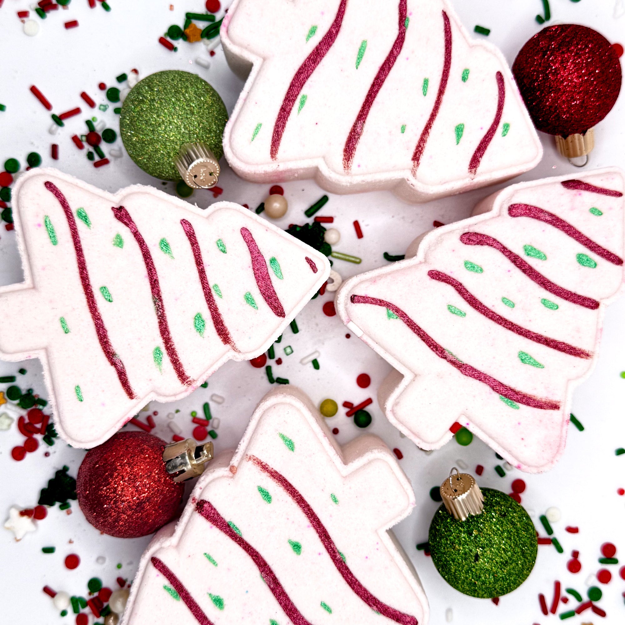 Decorative bath bombs shaped like Christmas trees with red and green icing on a festive background.
