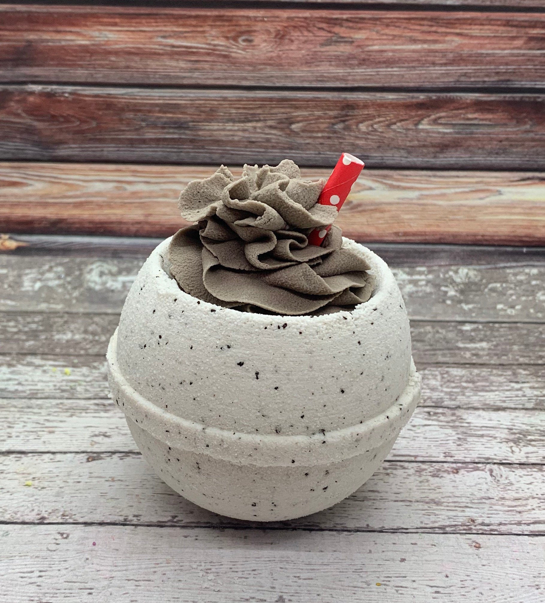 One coffee scent bath bomb with brown bubble frosting neatly piped on top and a red straw with polkadots in the top.