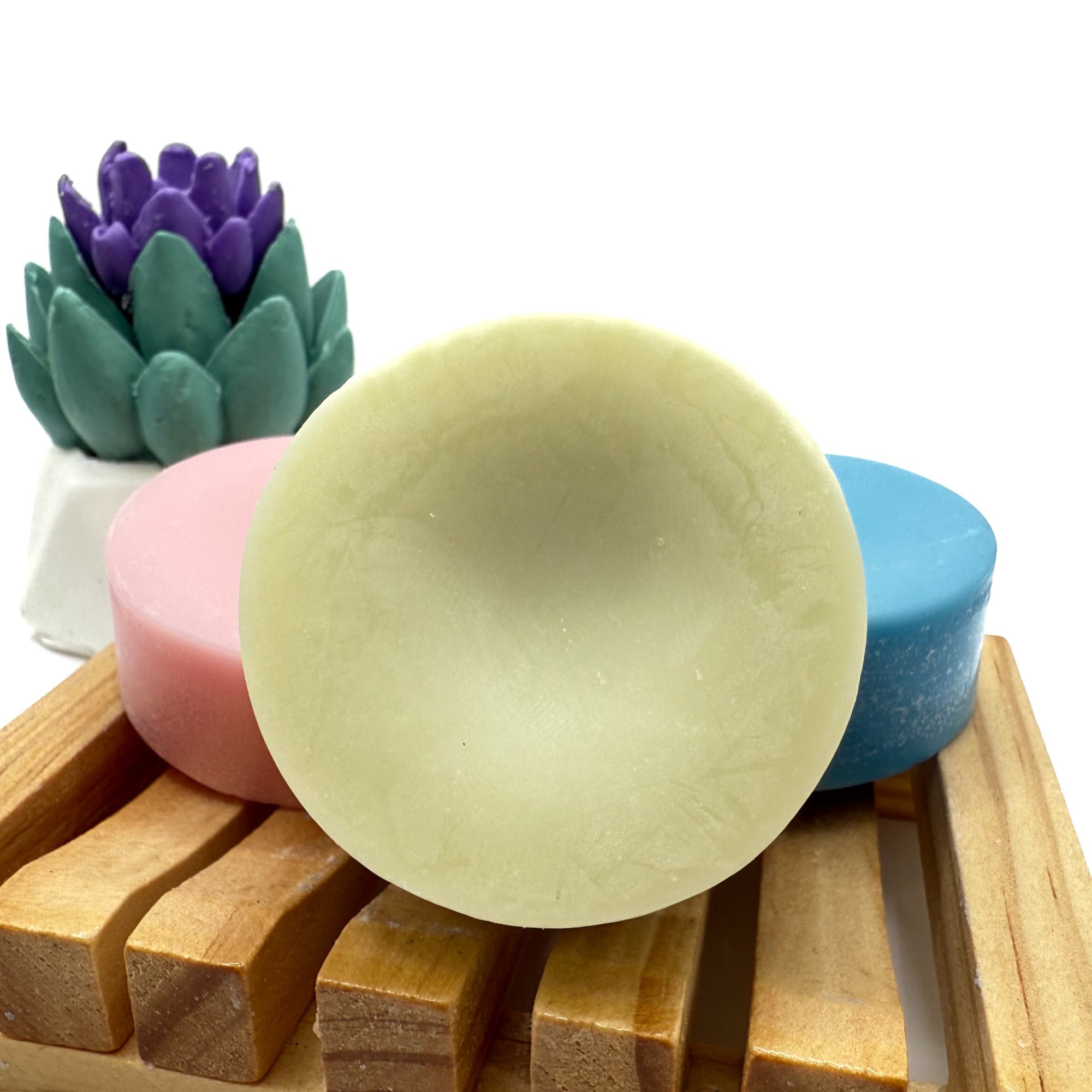 Round green conditioner bar for hair on wood soap lift with light pink and blue behind it.