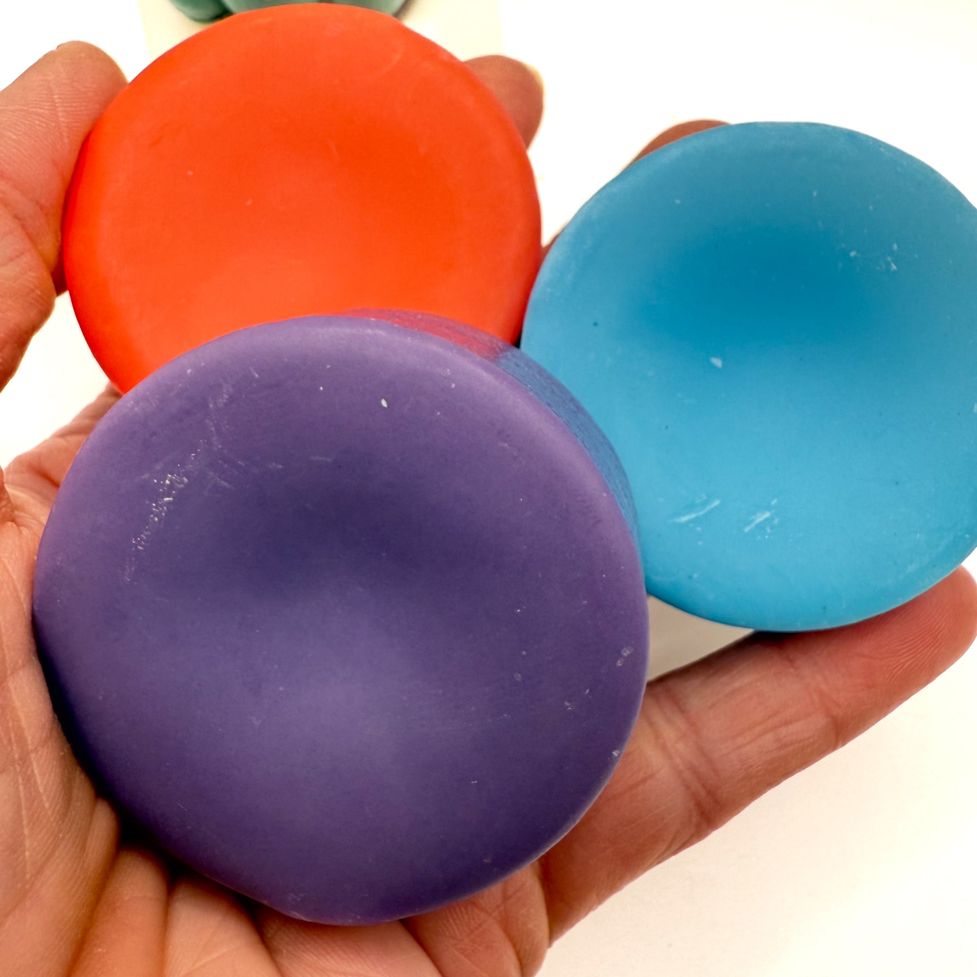 Purple, blue, orange solid conditioner bars held in a hand.
