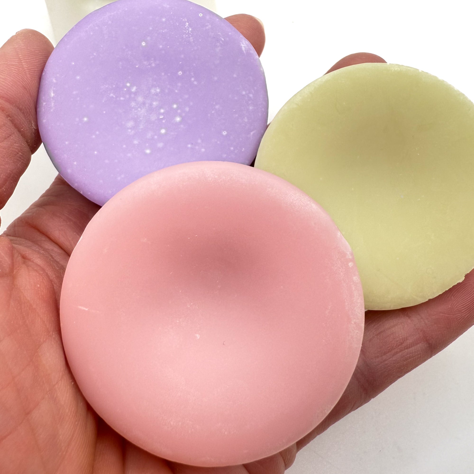 Purple, pink, green solid conditioner bars held in a hand.