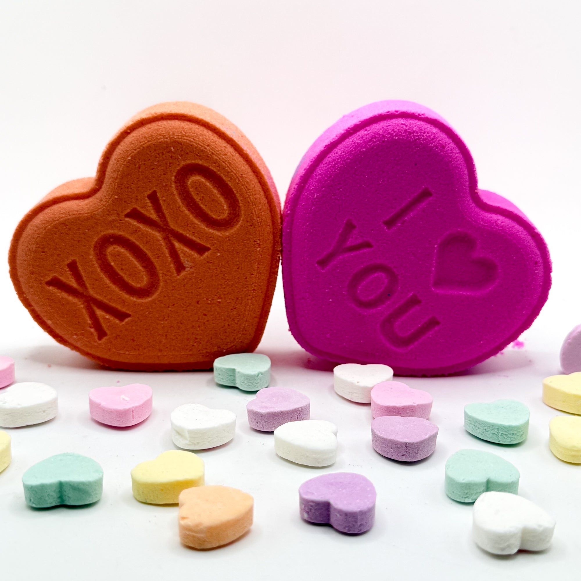 Pink and peach heart shaped conversation bath bombs with 'XOXO' and 'I love you' text on a white background.