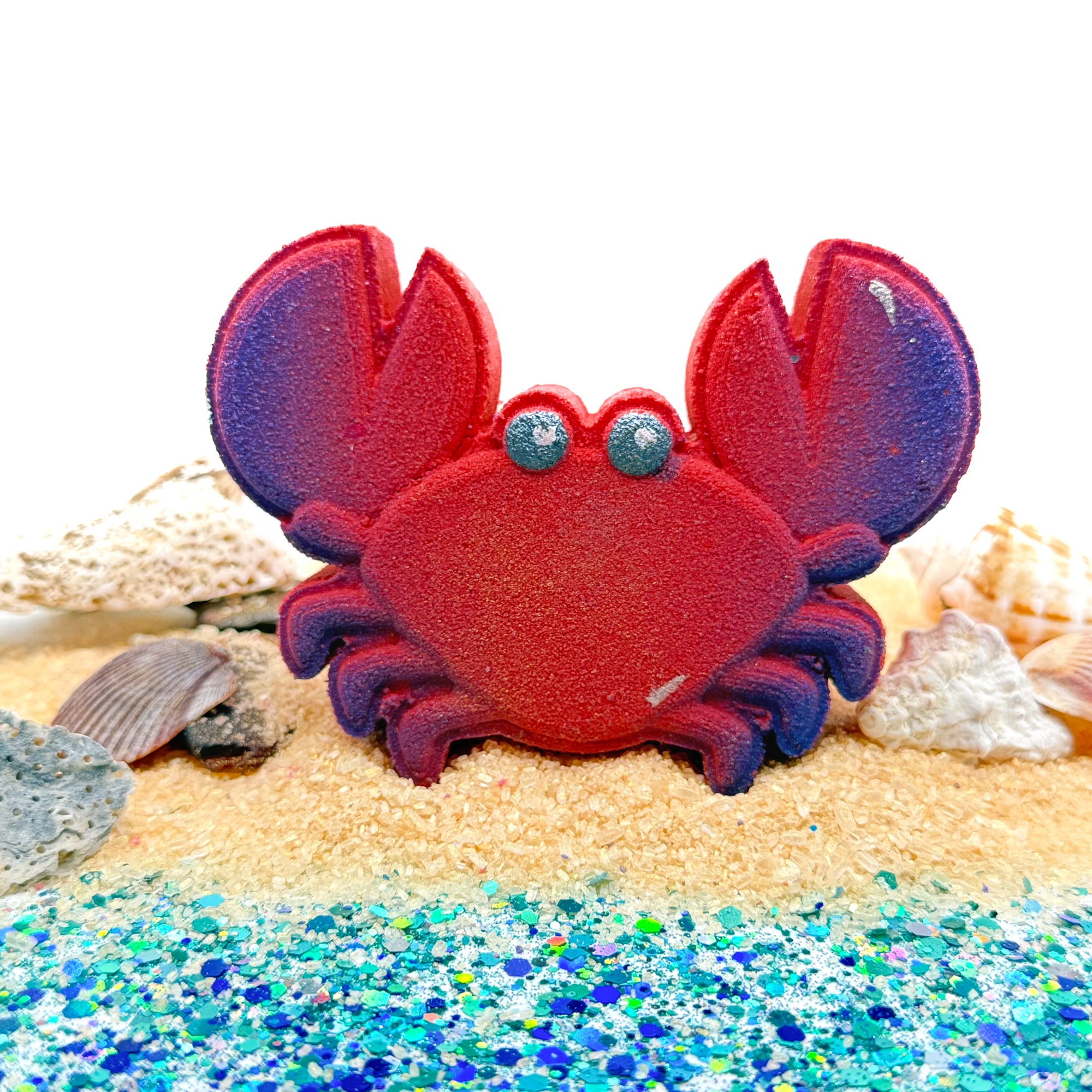 Handmade red crab bath bomb on a sandy surface with shells and glitter