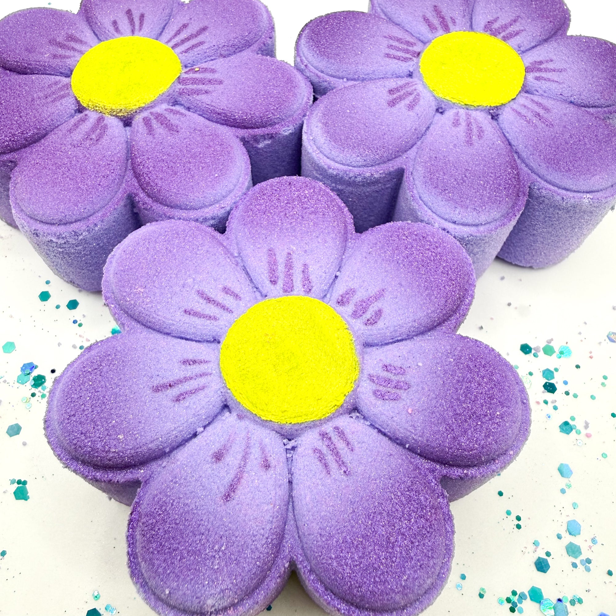 Purple daisy bath bombs with yellow centers on a white background