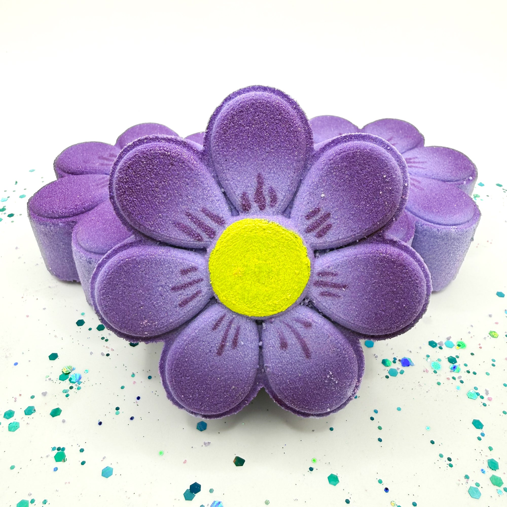 Hand made purple daisy bath bomb with a yellow center on a white background with colorful confetti.