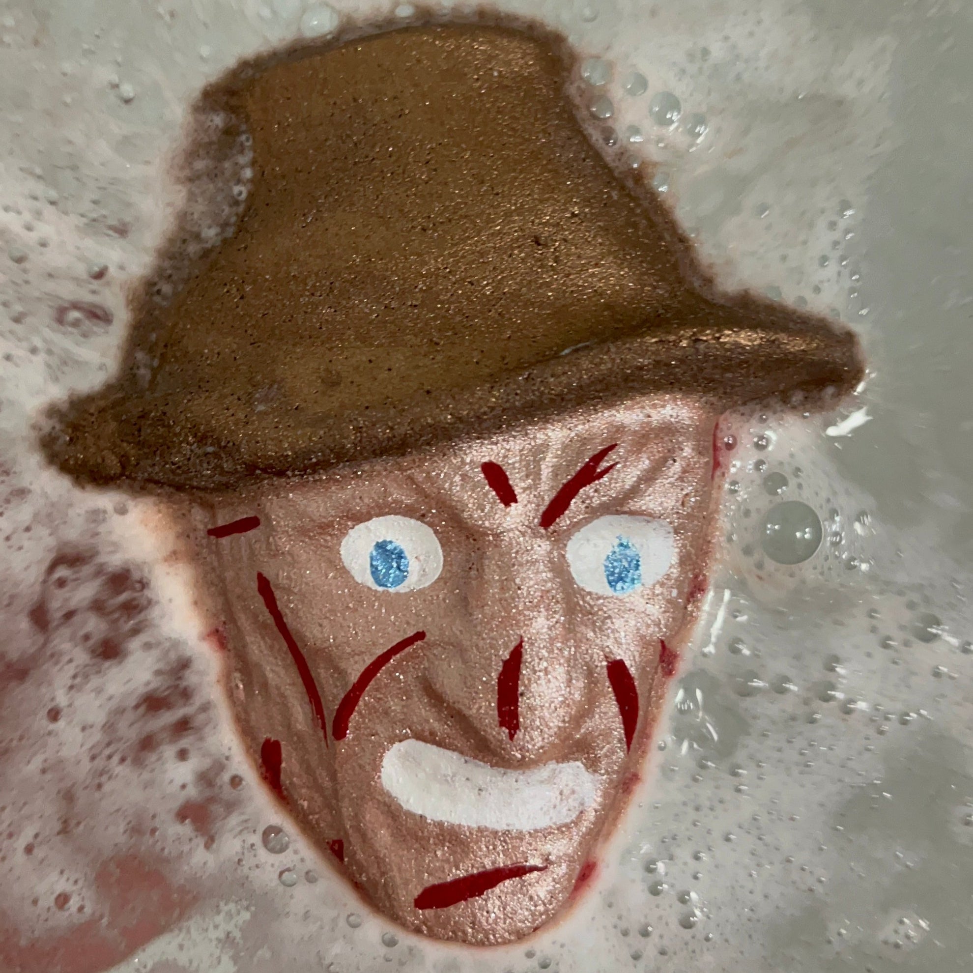 Dream Hunter horror movie-inspired bath bomb dissolving in water, releasing vibrant color swirls and fizz for a spooky bath experience.