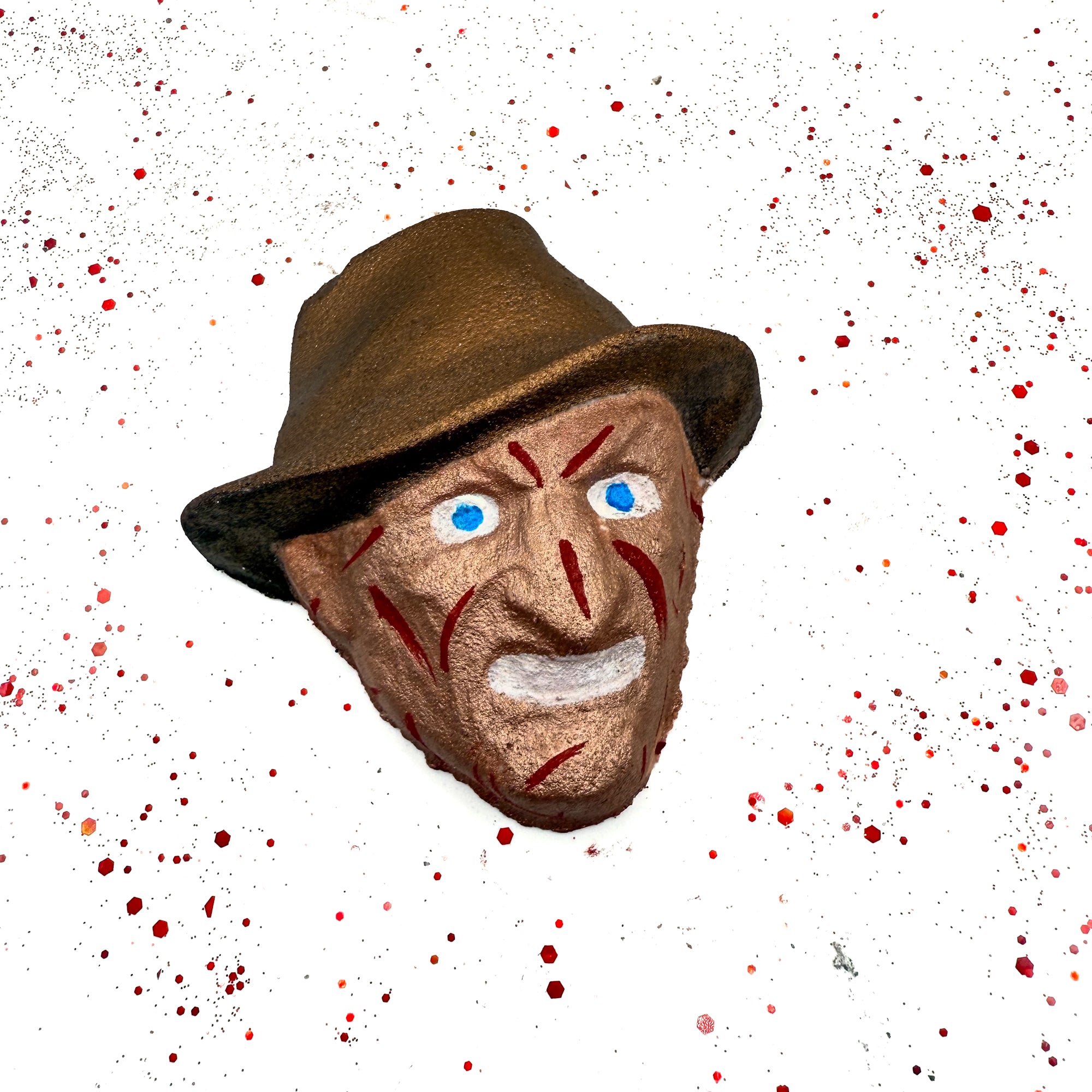Dream Hunter horror movie-inspired bath bomb with signature brown hat, scarred face, and blue eyes, displayed on blood-splatter background.