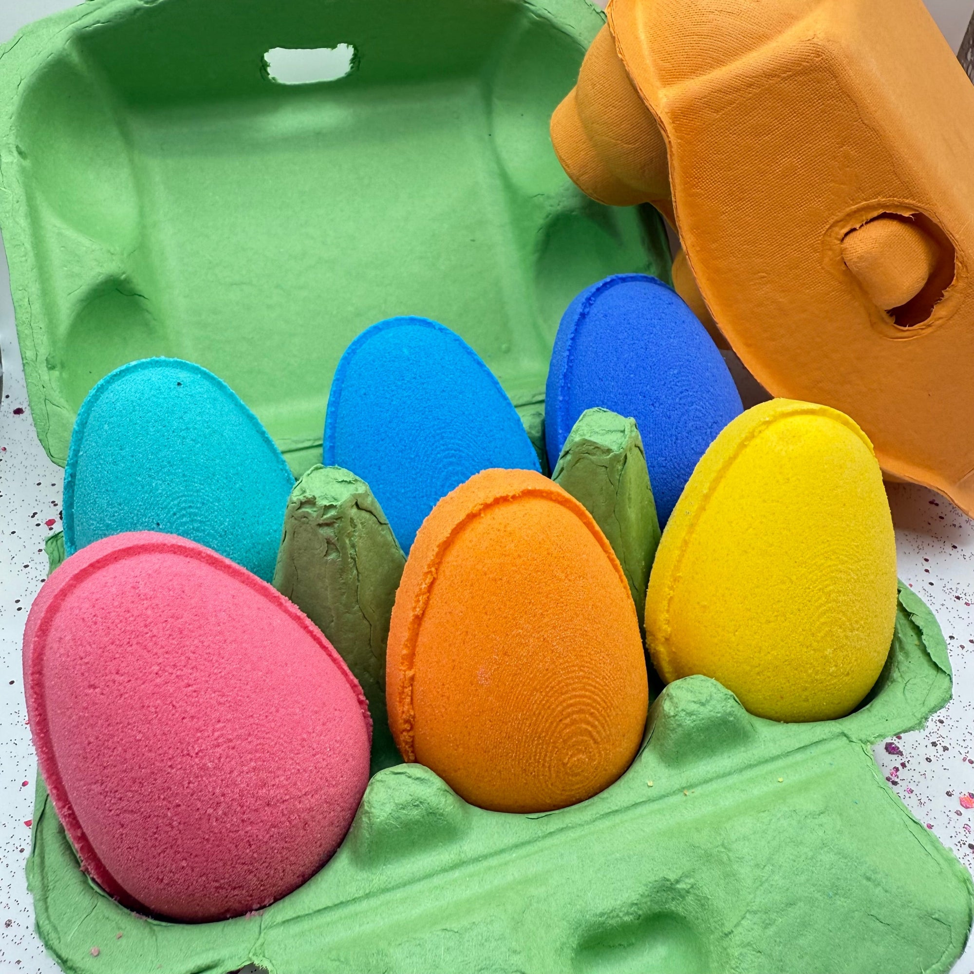 Six colorful egg shaped bath bombs for easter in a colorful egg carton made by Rusted Acre Soap Company.