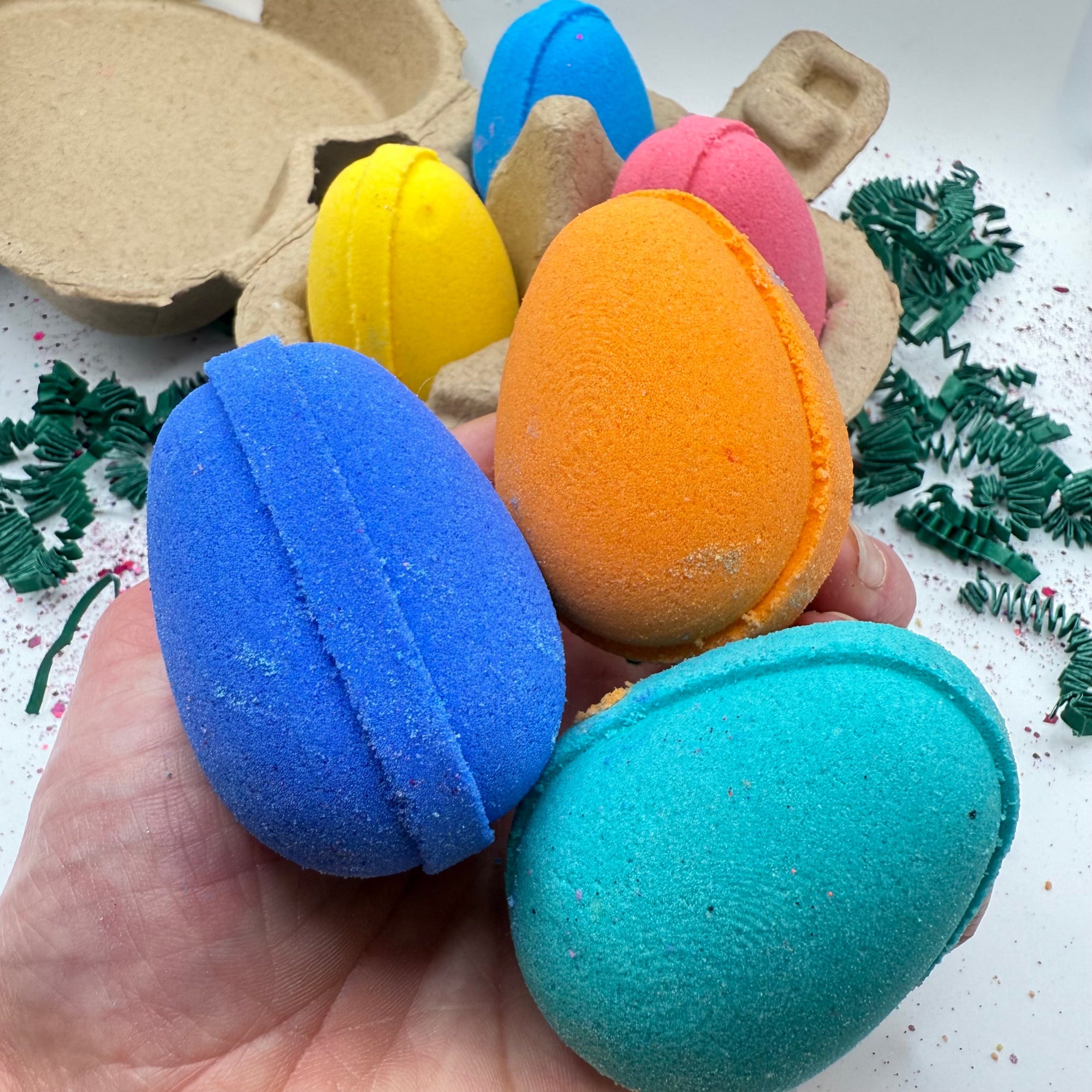 Three colorful egg shaped bath bombs displayed in a hand, made by Rusted Acre Soap Company.