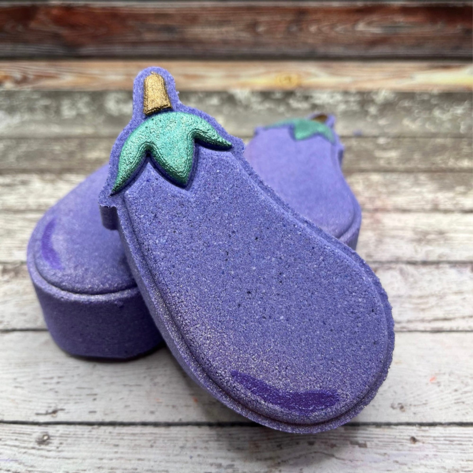 Hand painted eggplant bath bomb on Rustic wood background. Made by Rusted Acre Soap Co.