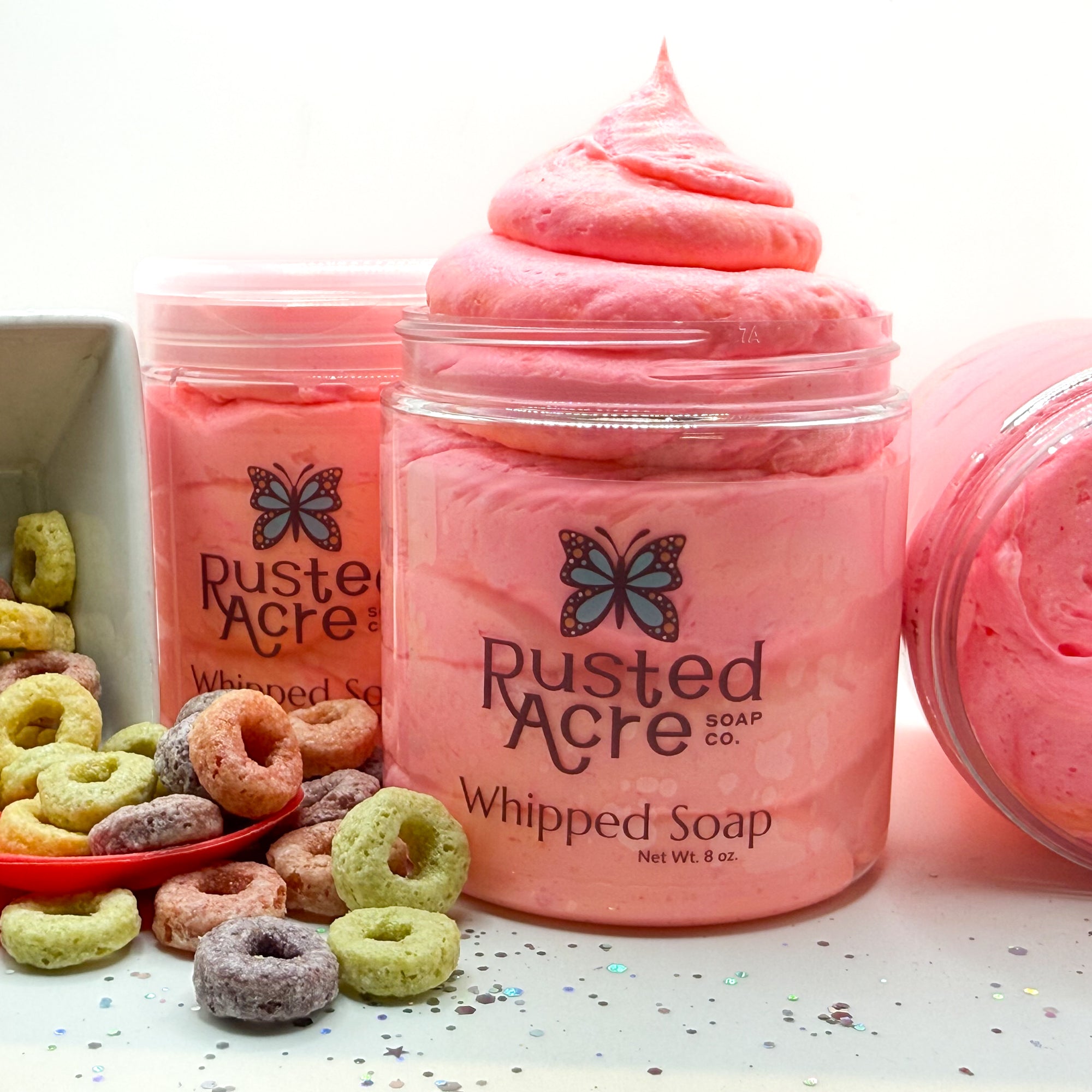 Jar of Rusted Acre Soap Company's vegan fruity cereal whipped soap. Pink and Orange soap in a reusable plastic jar in a lifestyle setting.