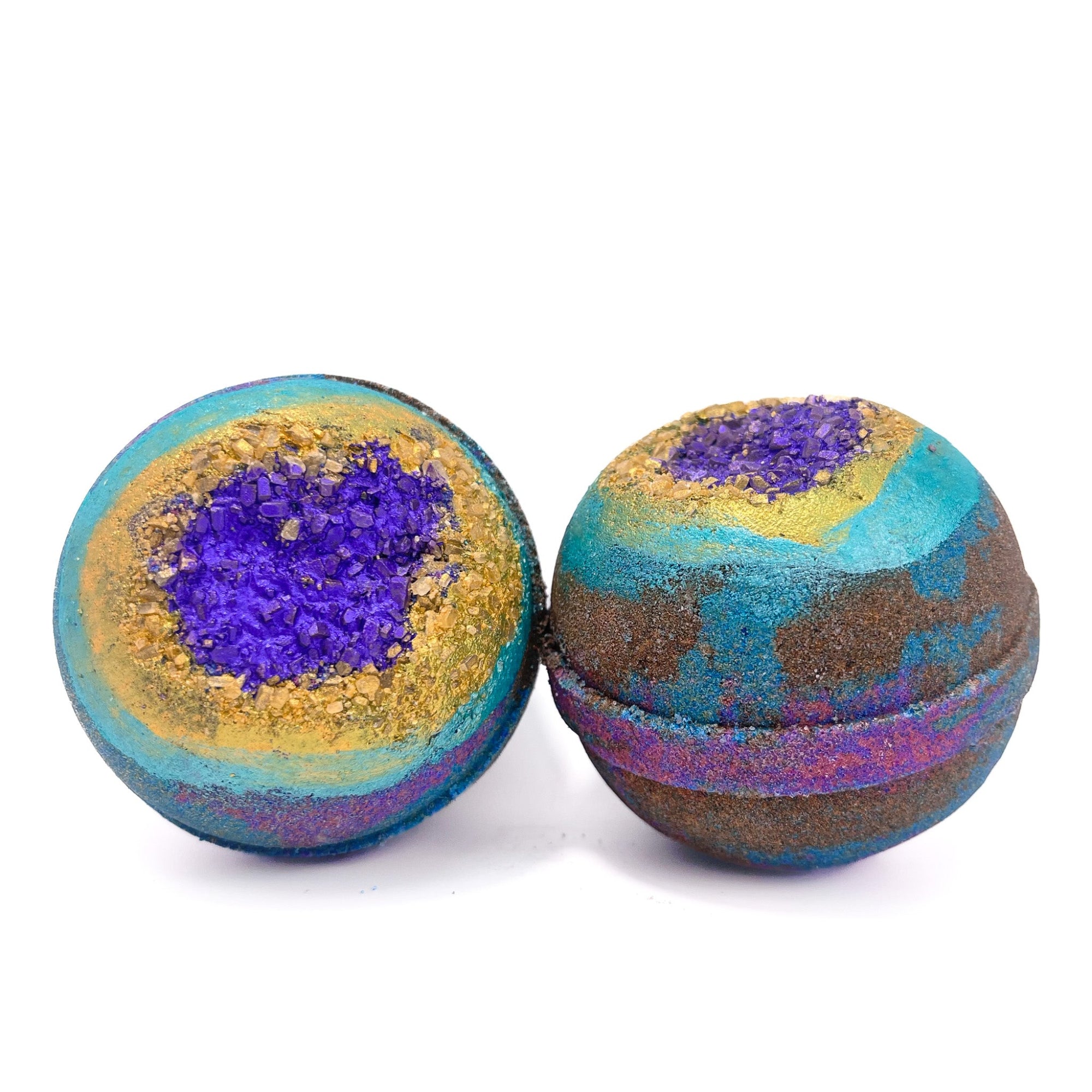 Two dark colored round bath bombs with Epsom salt embedded into the top. Dusted purple and hand-painted gold and teal rings