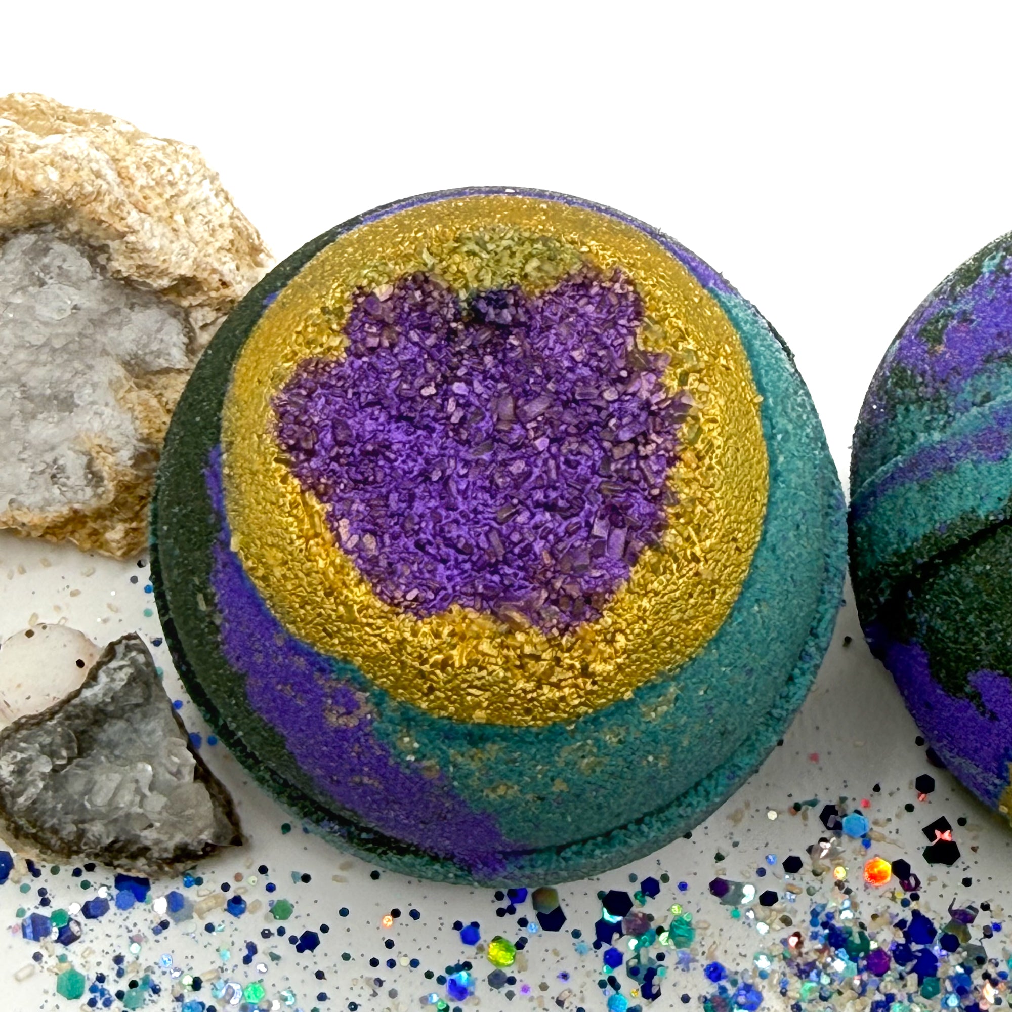 Round bath bomb swirled with black and teal embedded with gold sea salt.
