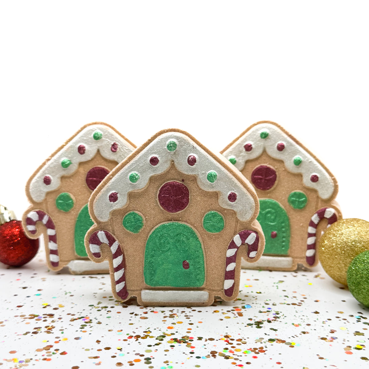 Three hand painted gingerbread house bath bombs on a white background.