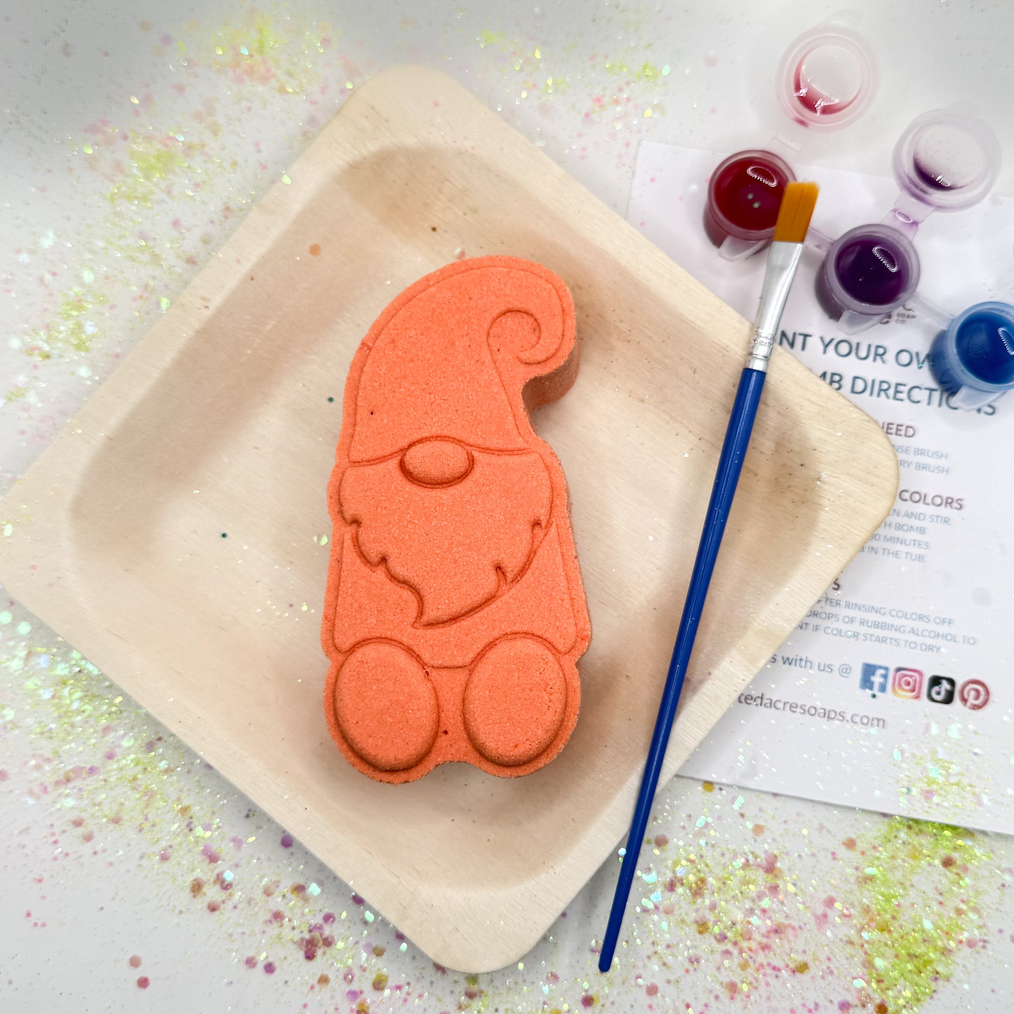 Orange paint your own gnome bath bomb kit on a wood tray with a paintbrush and color swatches.