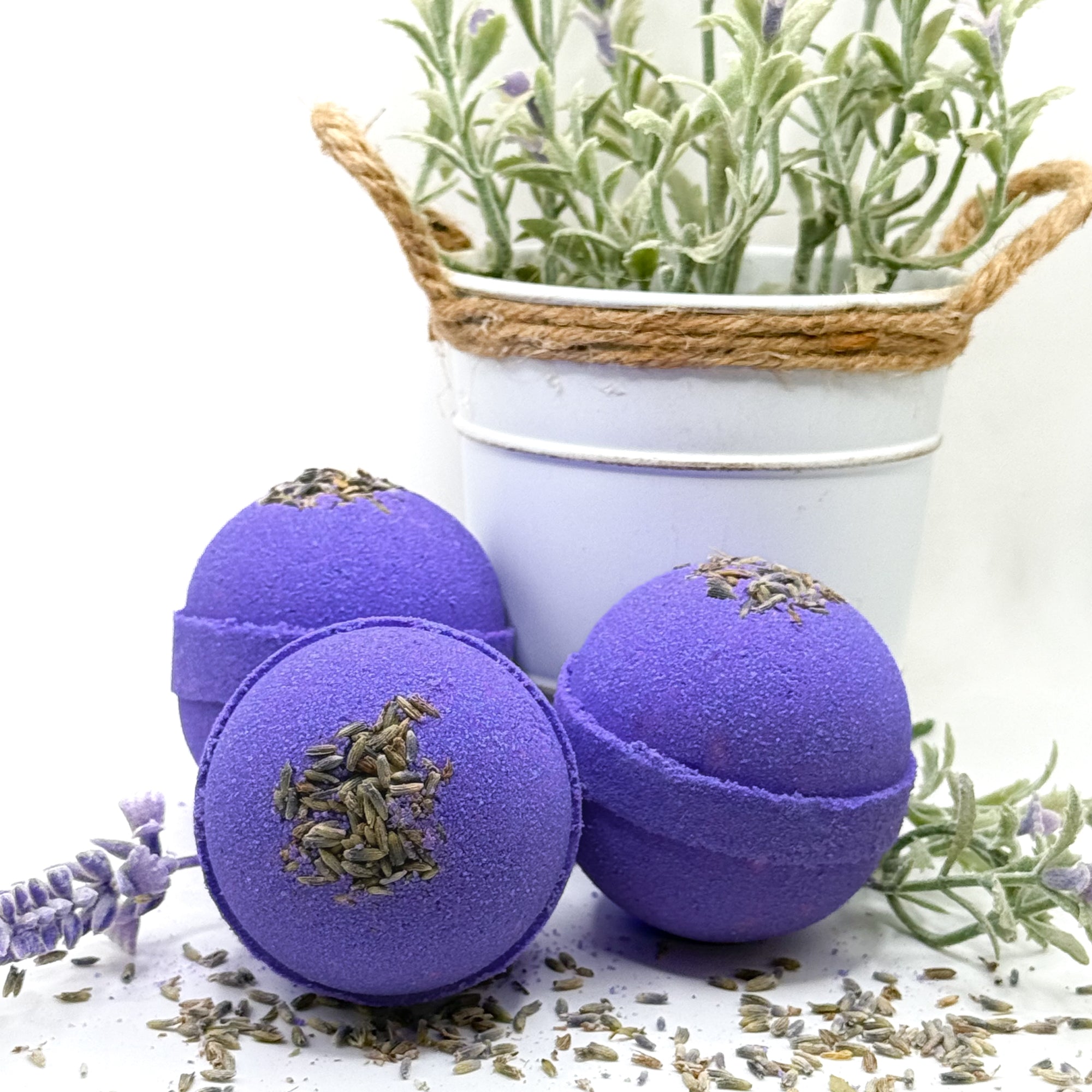 Purple lavender bath bombs with lavender flowers on a white surface with a potted lavender plant in the background.