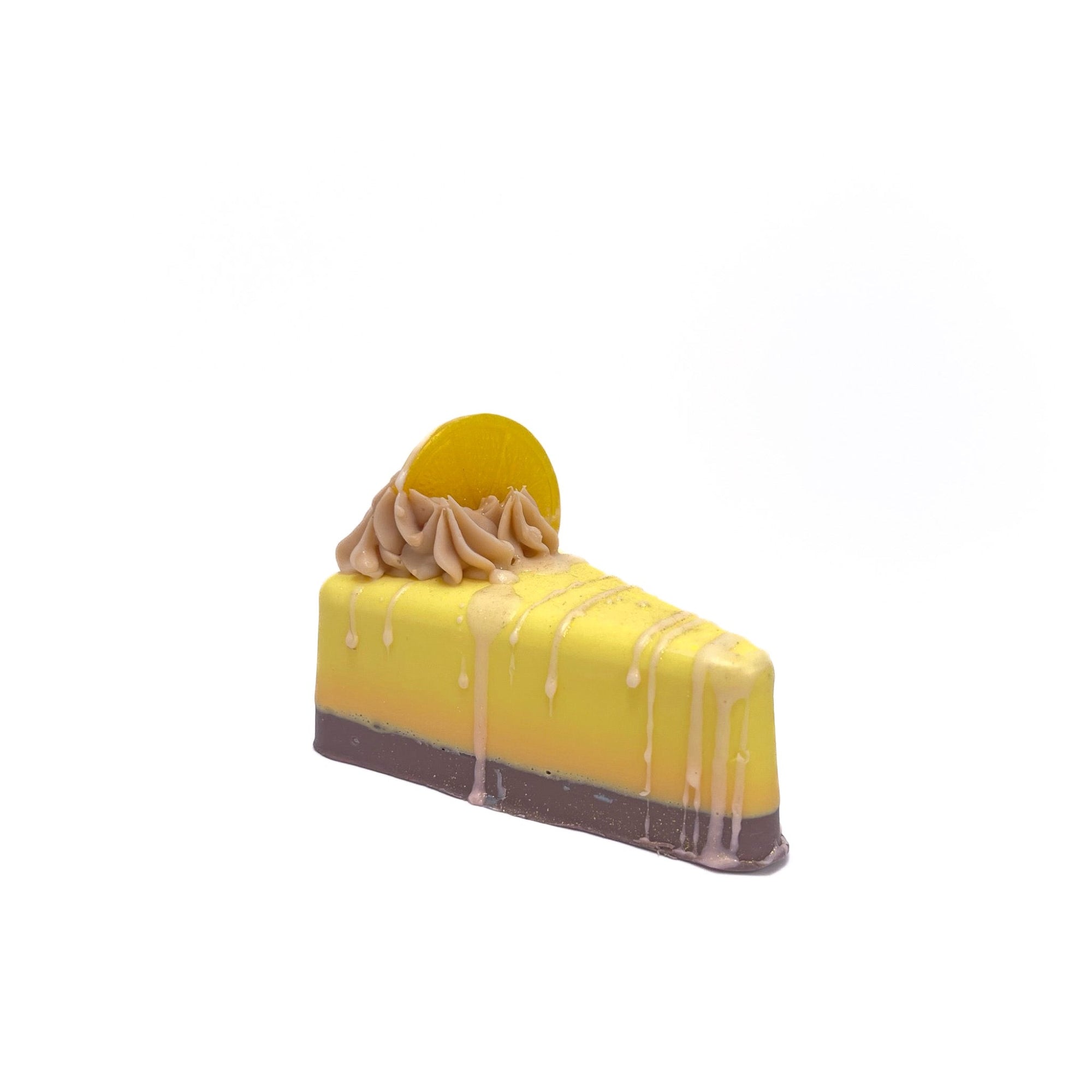 Pie slice shaped lemon soap topped with soap frosting and a slice of lemon shaped soap and white drizzle. The body is yellow, the frosting is cream color.