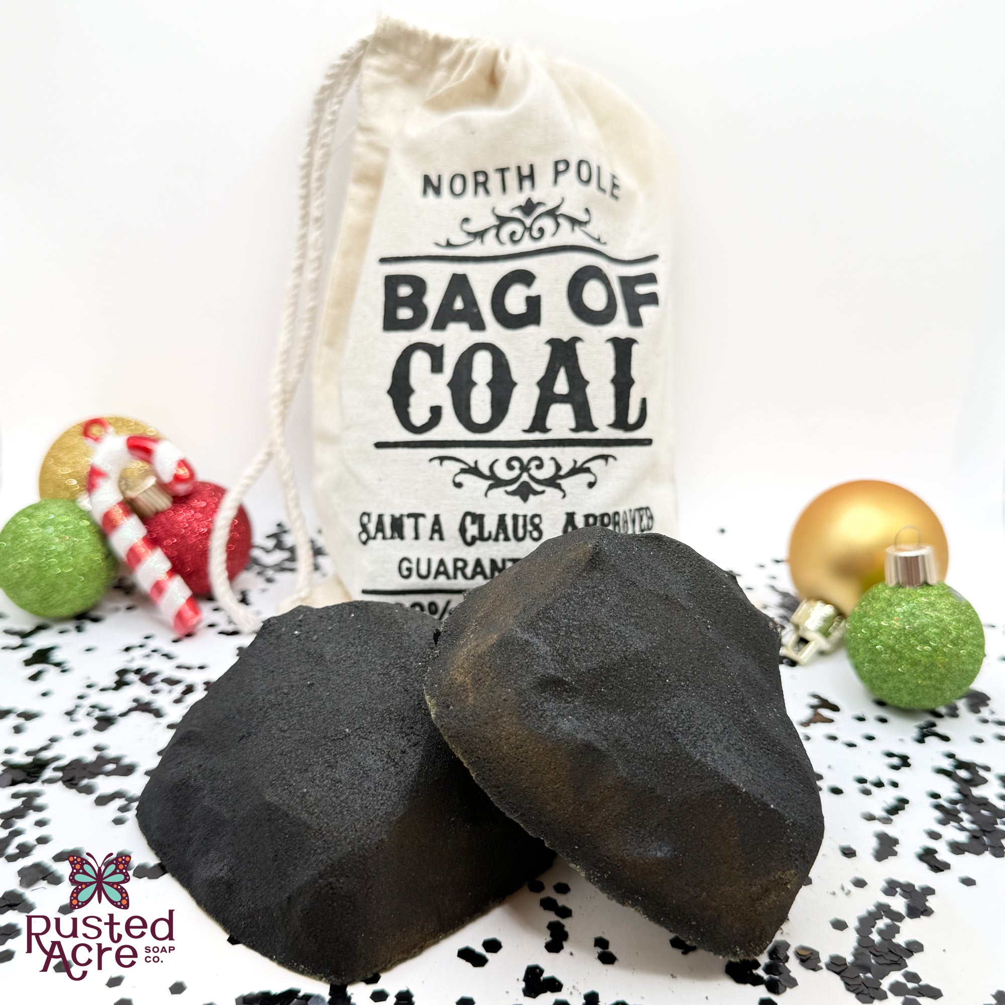 Two black lumps of coal bath bombs with a tan canvas "bag of coal" on a festive background handmade by Rusted Acre Soap Co.