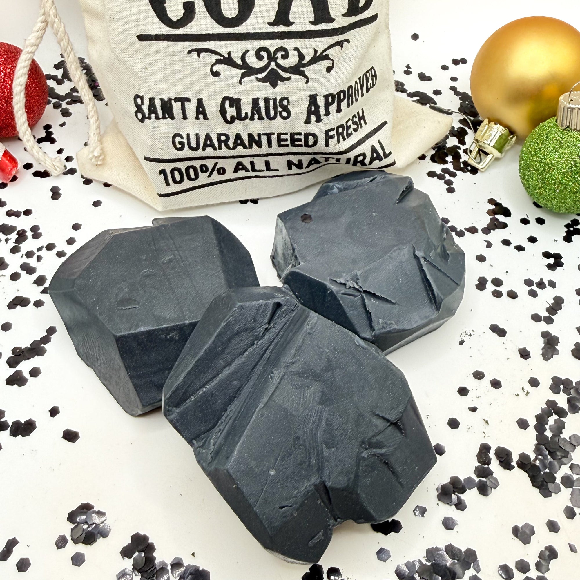 Three black lumps of coal soap with tan canvas "Bag of Coal" with Christmas decorations.