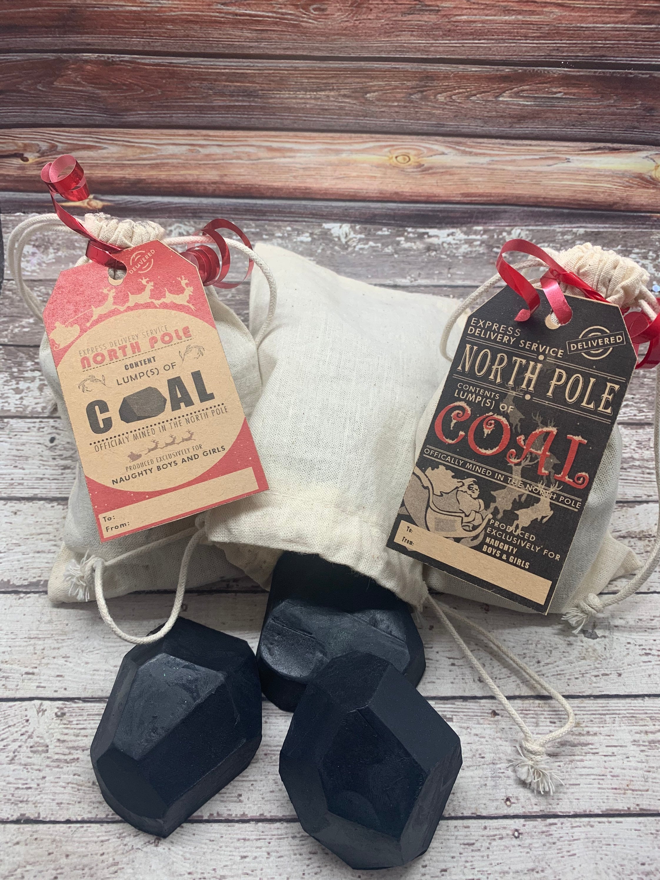 Three lump of coal shaped soaps spilling from light colored canvas bag on rustic wood background.