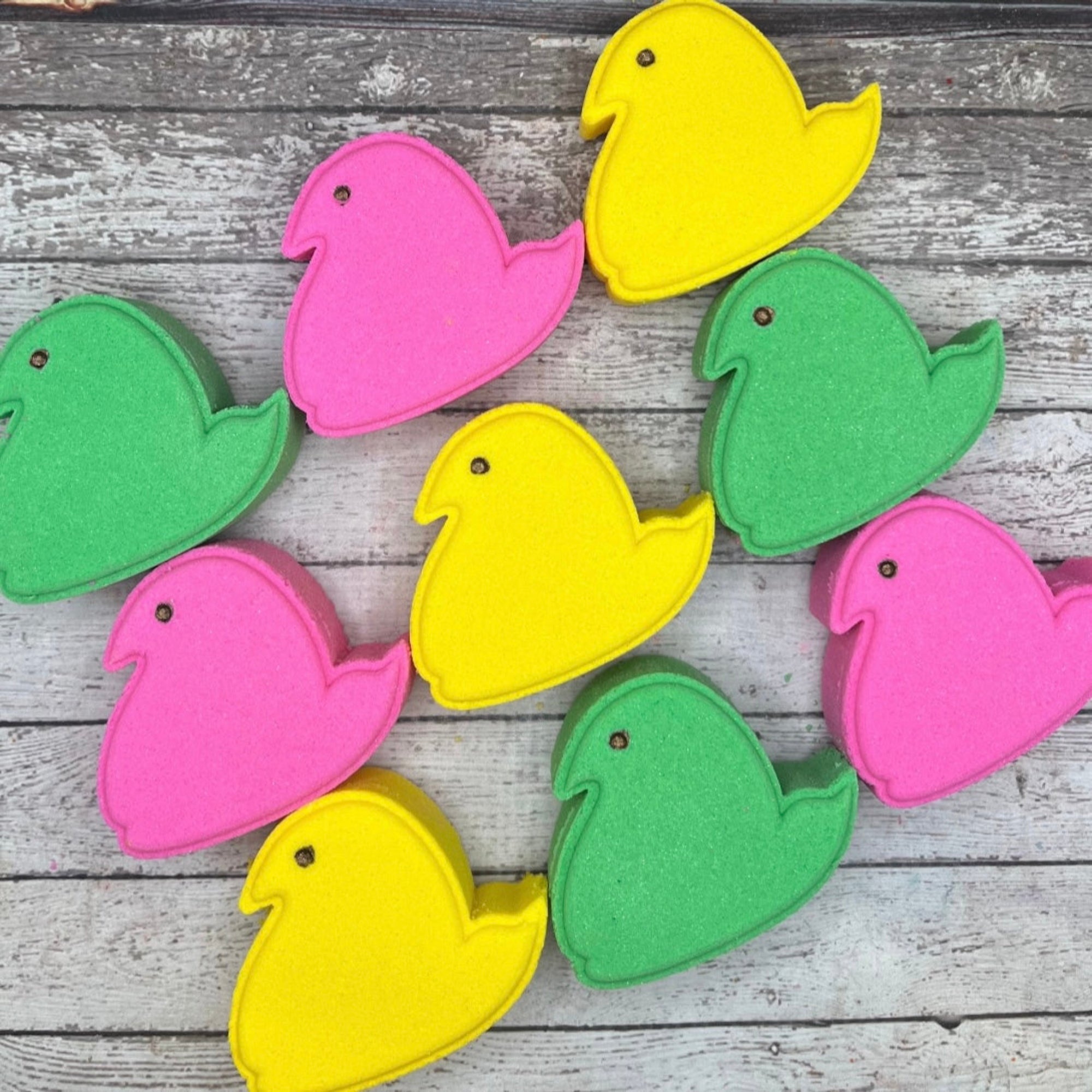 Multiple colors of Rusted Acre Soap Companies marshmallow chick bath bombs lined up on a rustic wood background.