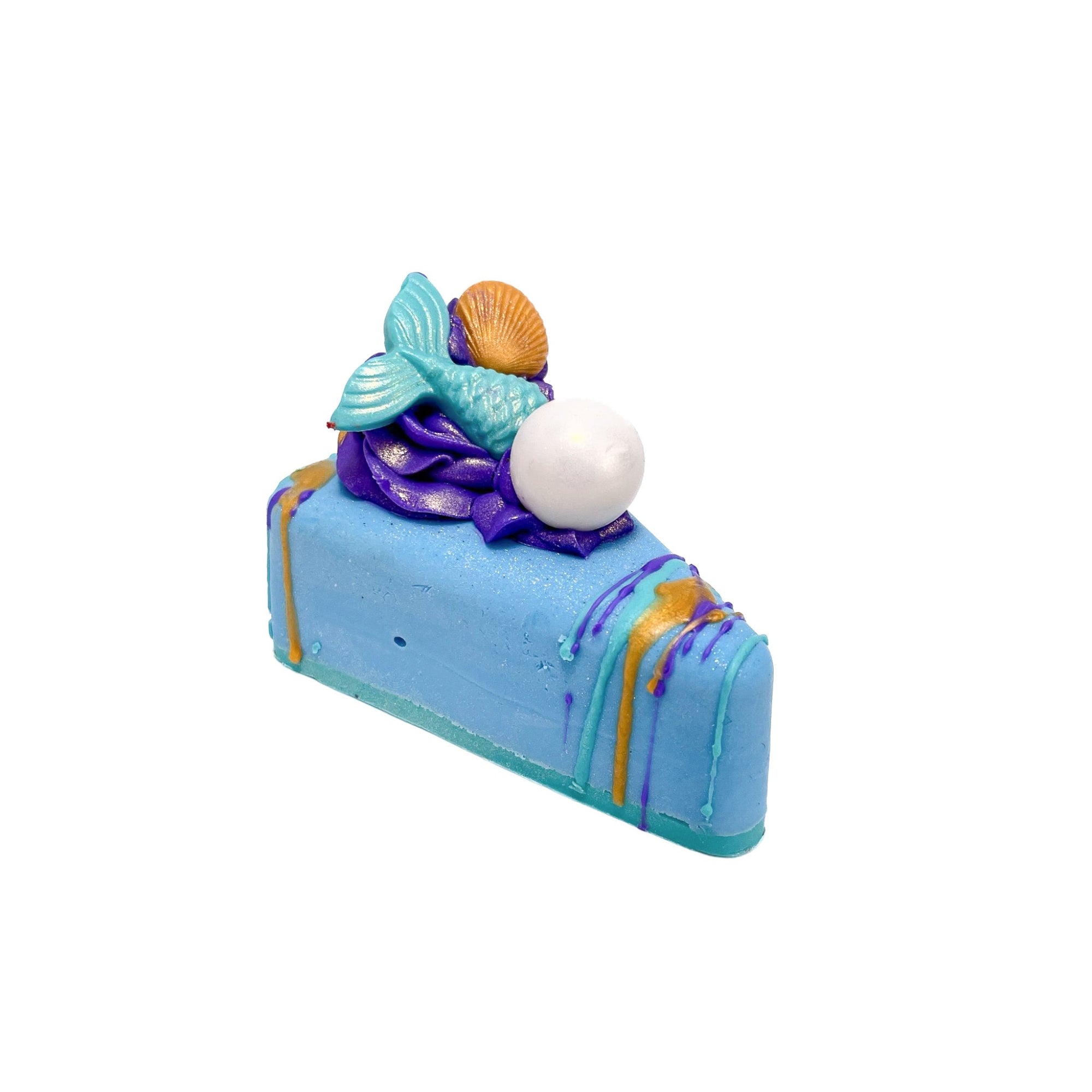 A blue pie slice shaped bar of soap. Topped with a puff of soap, a mermaid teal mermaid tail soap embed, a white pearl soap embed, drizzled with teal, purple, and gold soap.