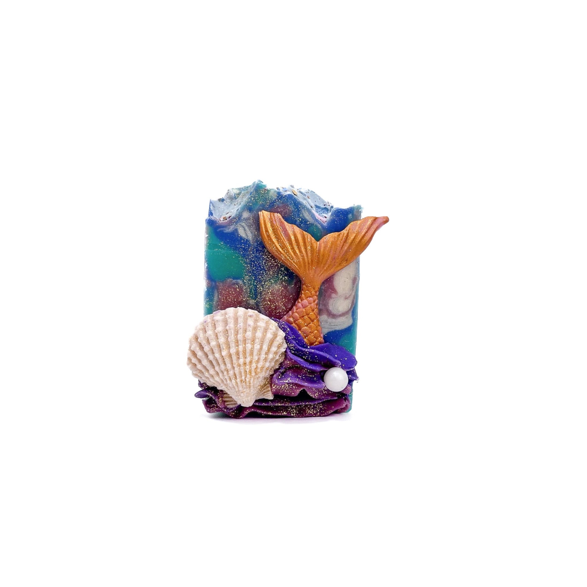 A bar of Rusted Acre Soap Company's Mermaid Tail handmade soap. Swirled teal, blue, and pink. A pink mermaid tail, cream colored clam shell, and pearl soap embed on front.
