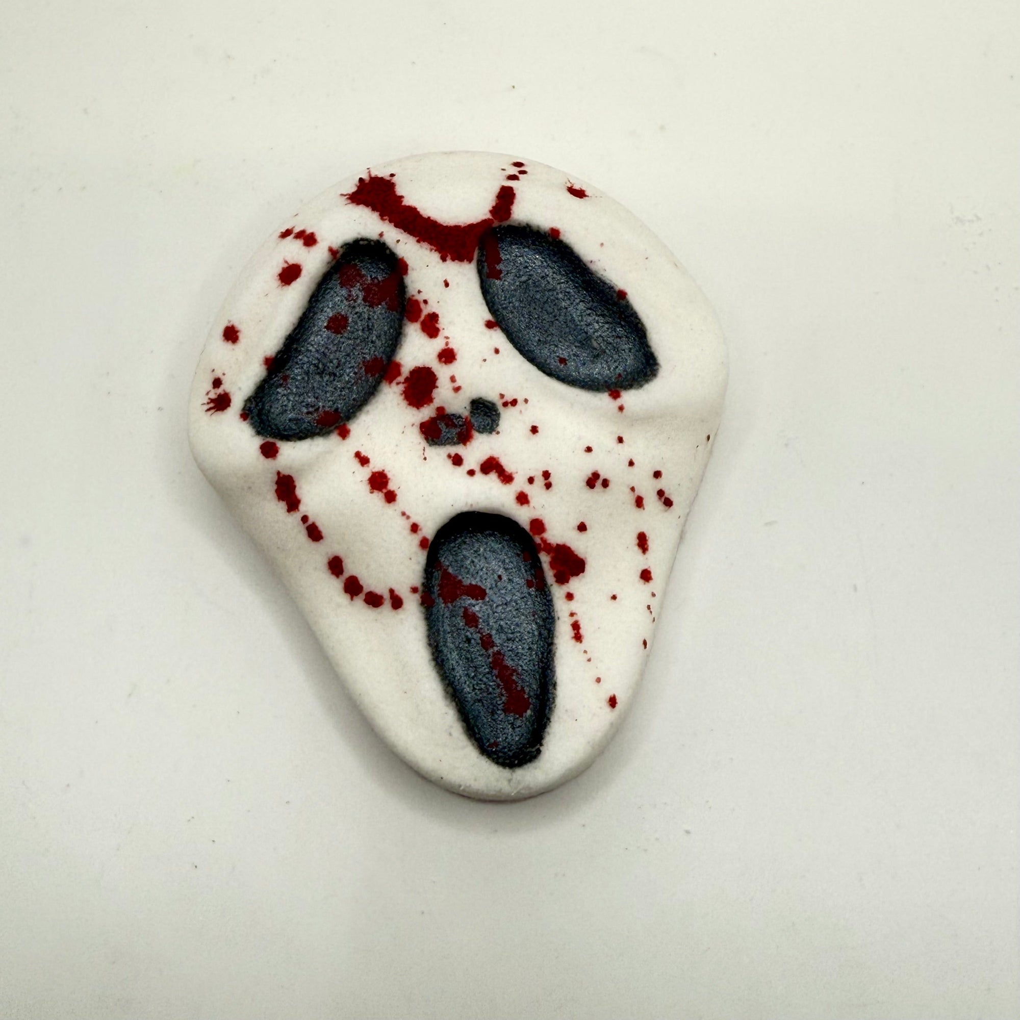 A white horror inspired handmade bath bomb hand-painted black eyes and nostrils splattered with red blood.