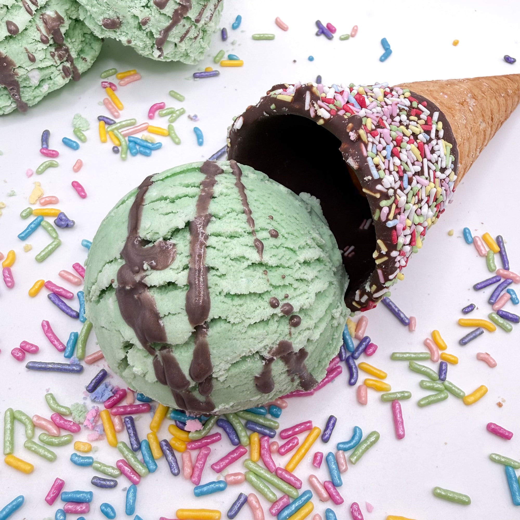 A scoop of mint green bubble bath scoop resembling a scoop of ice cream with a chocolate covered cone and rainbow sprinkles handmade by Rusted Acre Soap Co.