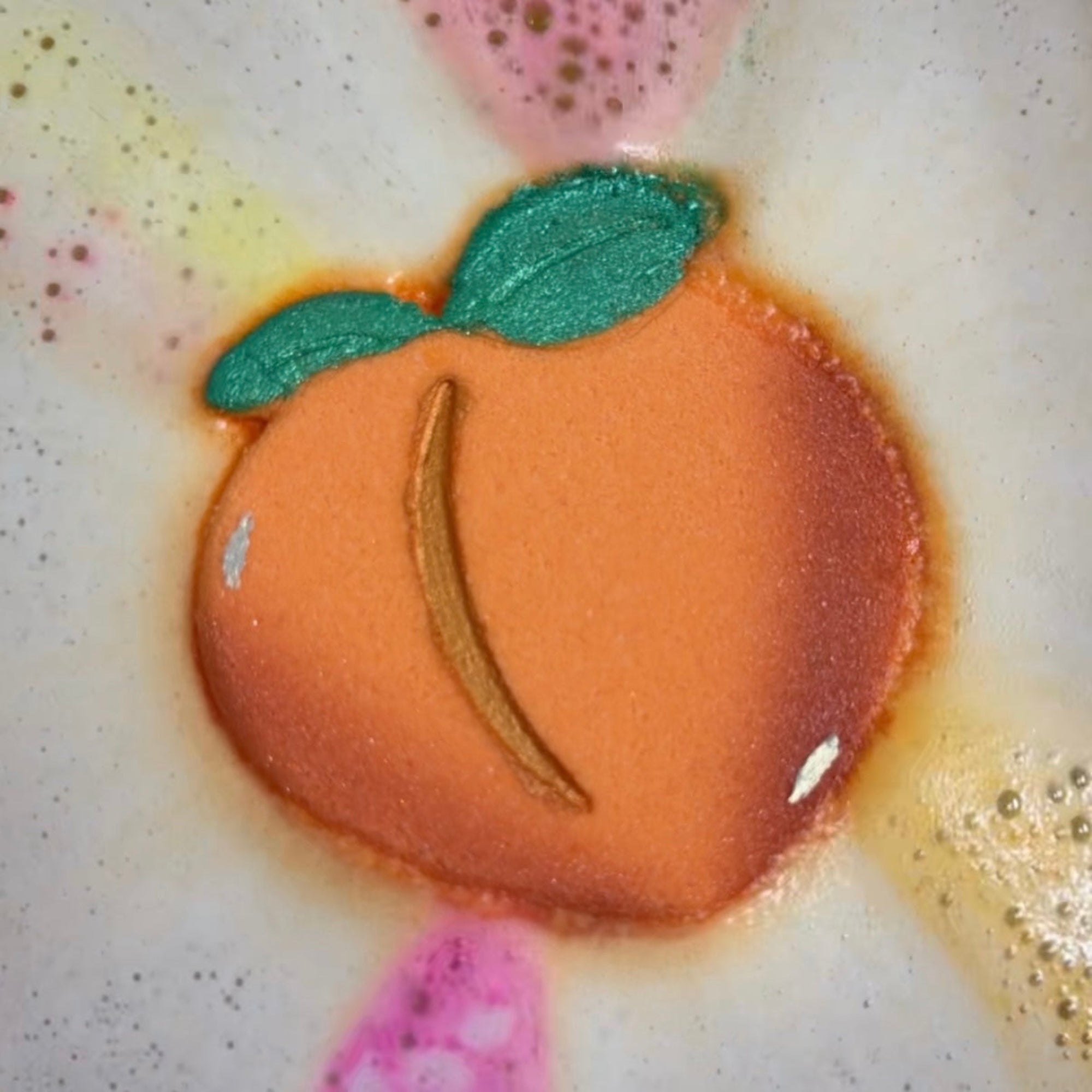 Peach bath bomb dissolving in the water with pink, yellow and orange colors shooting out.
