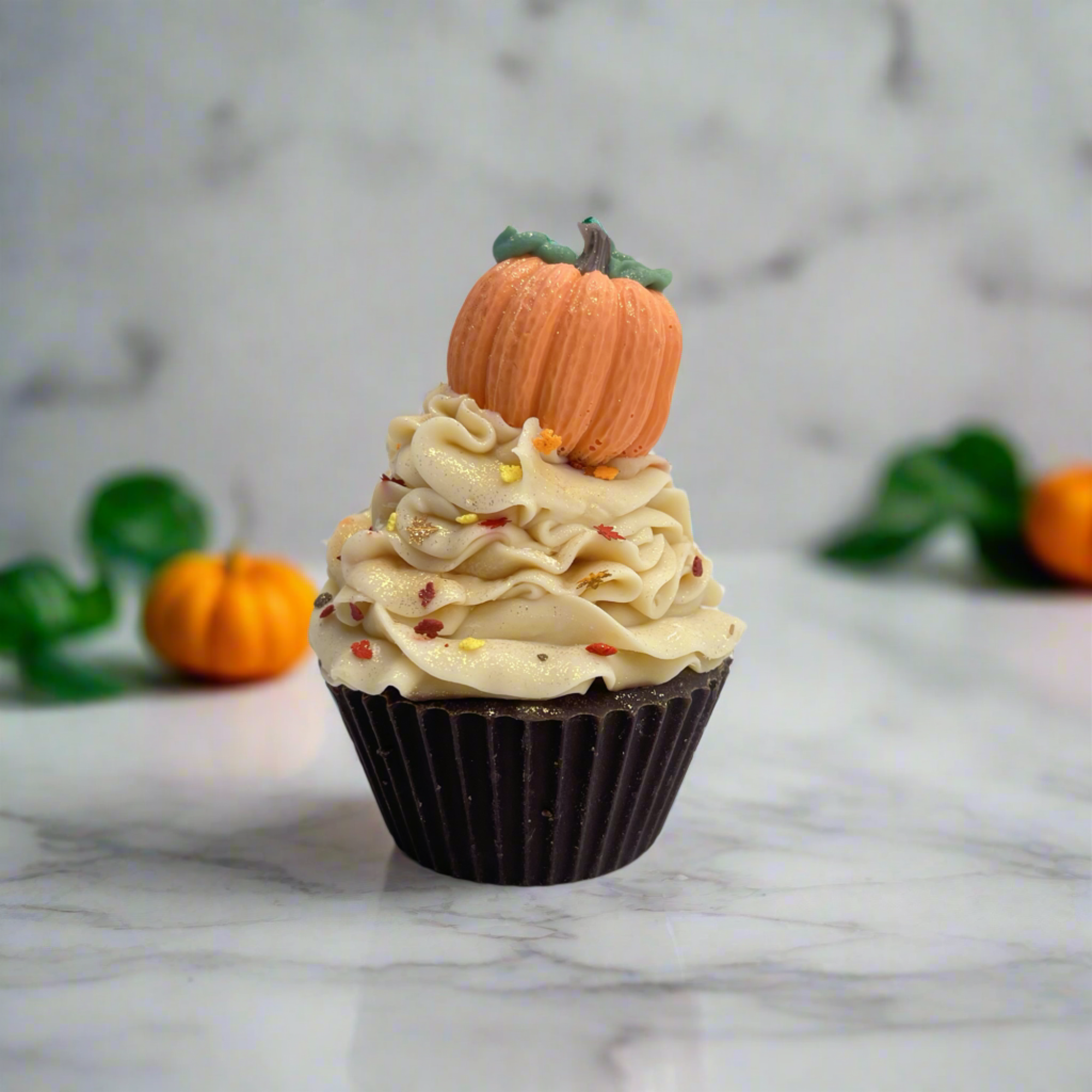 A cupcake bar soap with chocolate brown cake, light tan frosting, topped with orange pumpkin soap embed.