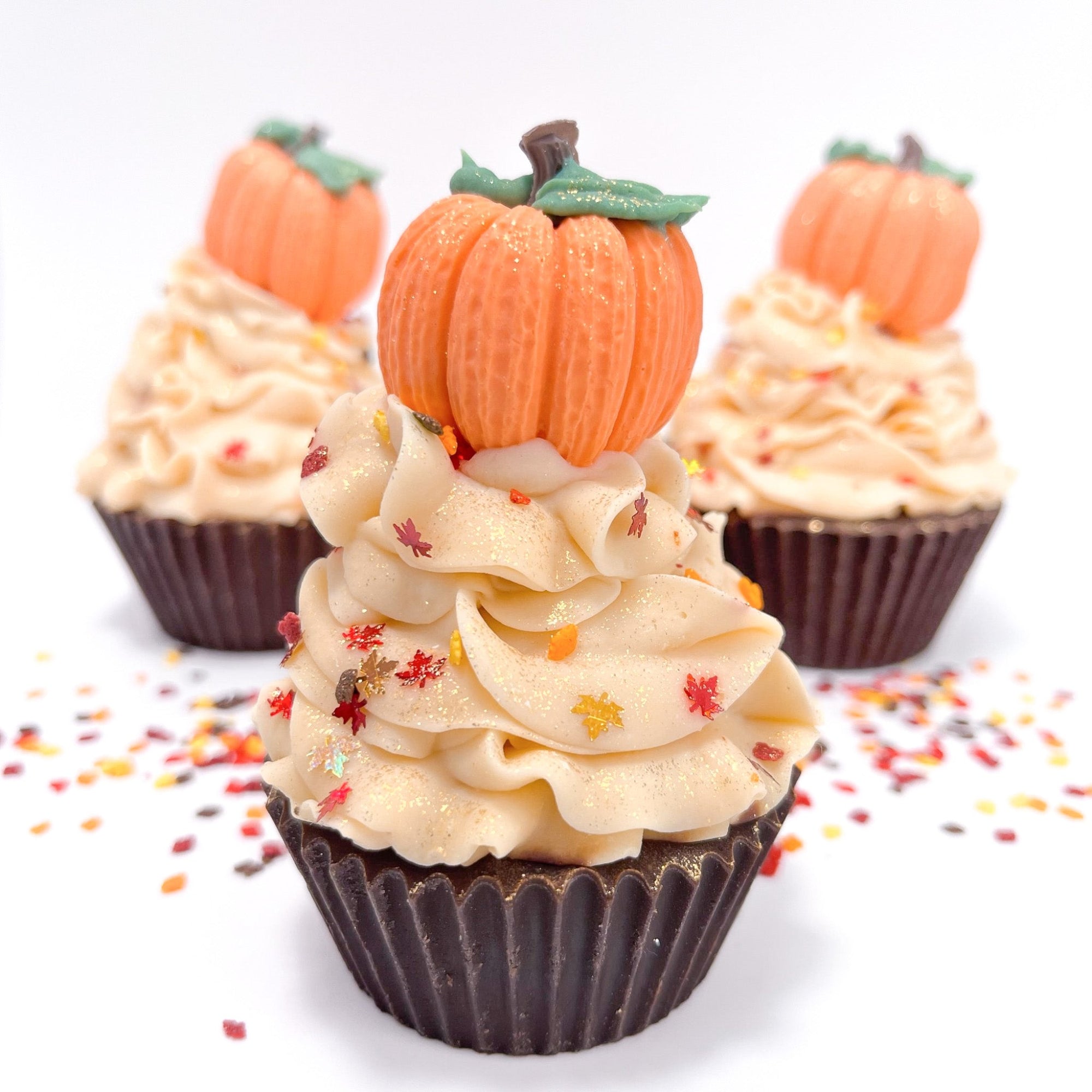 Three fall themed cupcake soaps scented with pumpkin spice. Dark brown cake, cream colored frosting, topped with an orange pumpkin soap and fall leaf sprinkles.